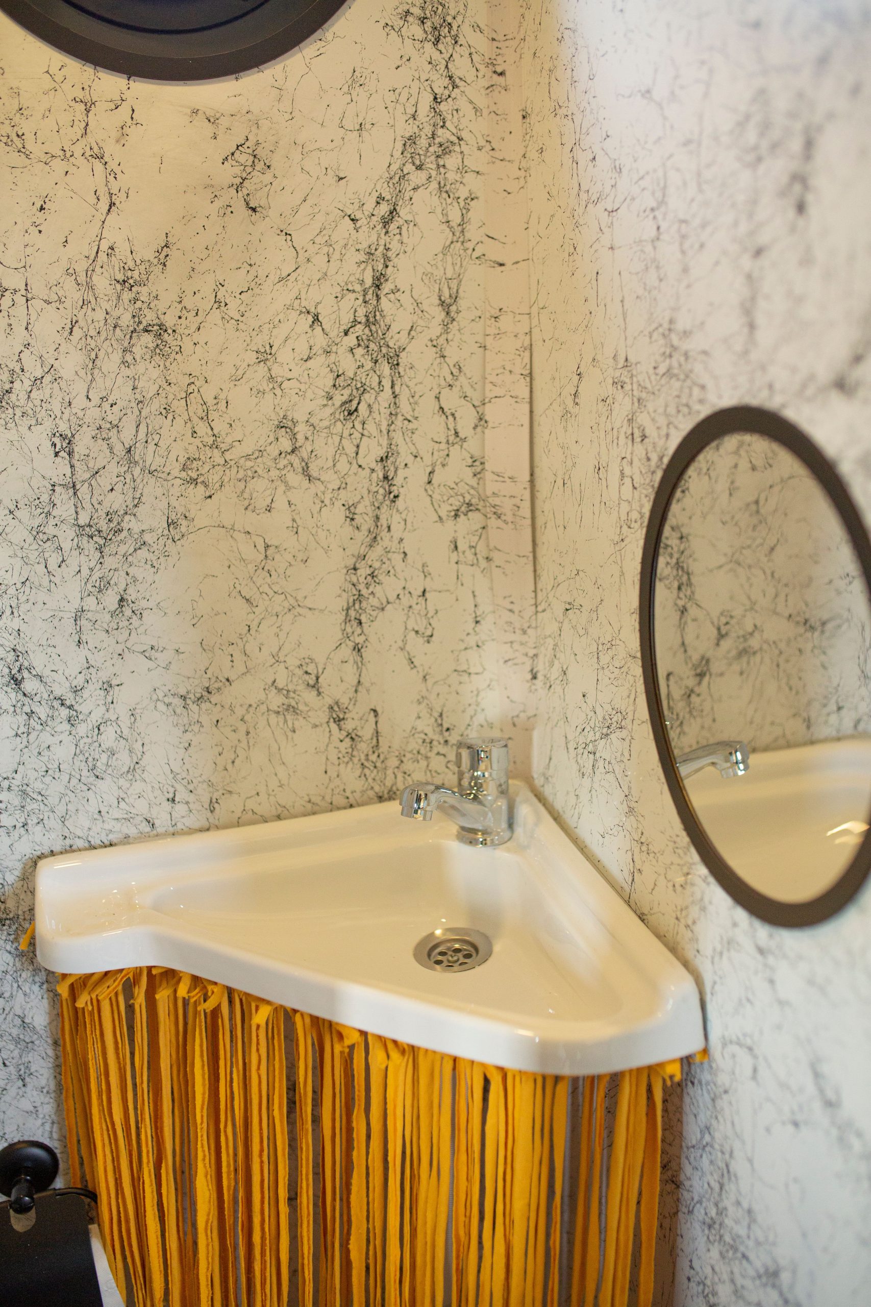 Elegant corner bathroom sink with a round mirror and marble textured walls.