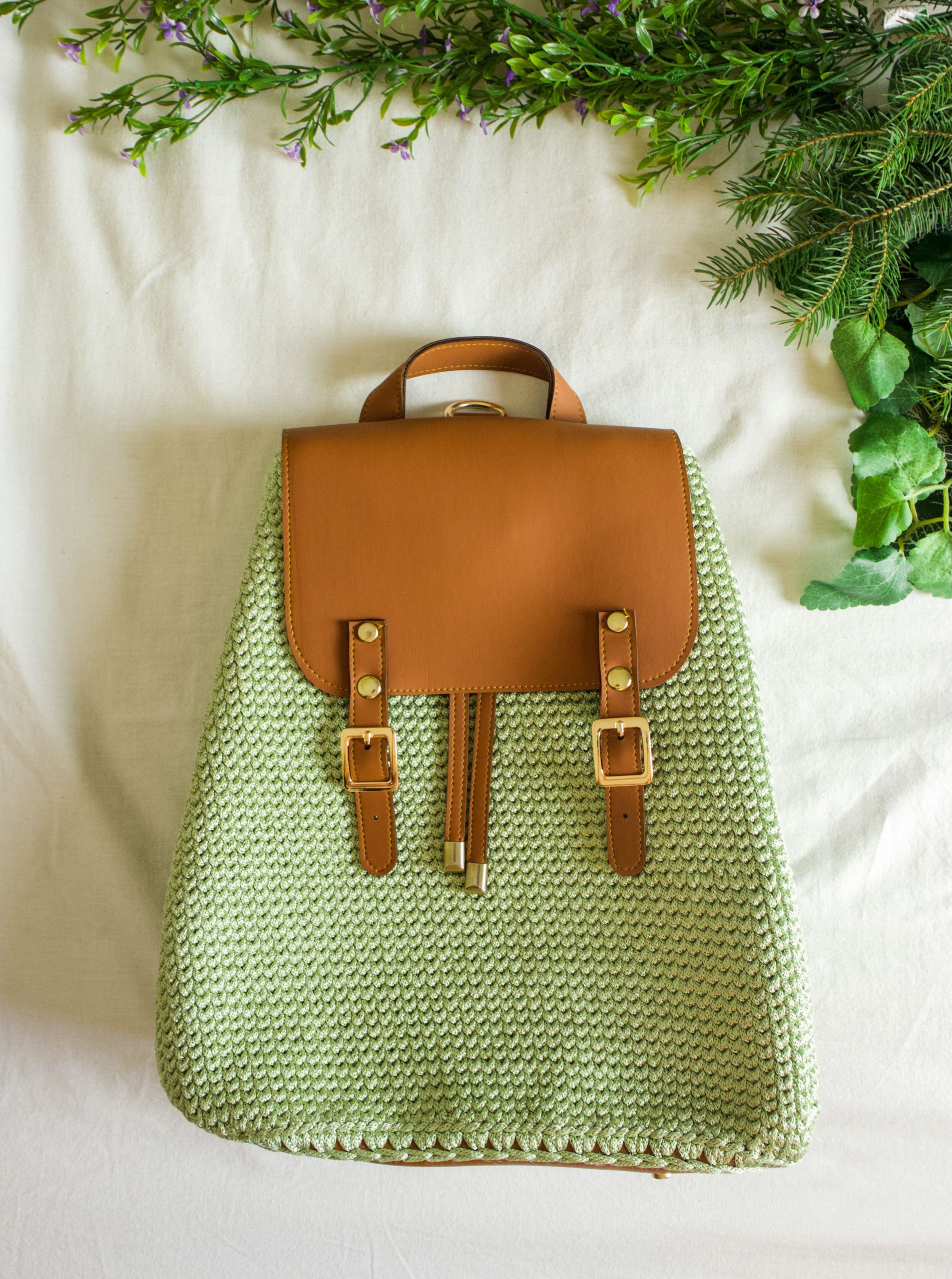 Elegant hand-crocheted backpack with leather accents on a nature-inspired background.