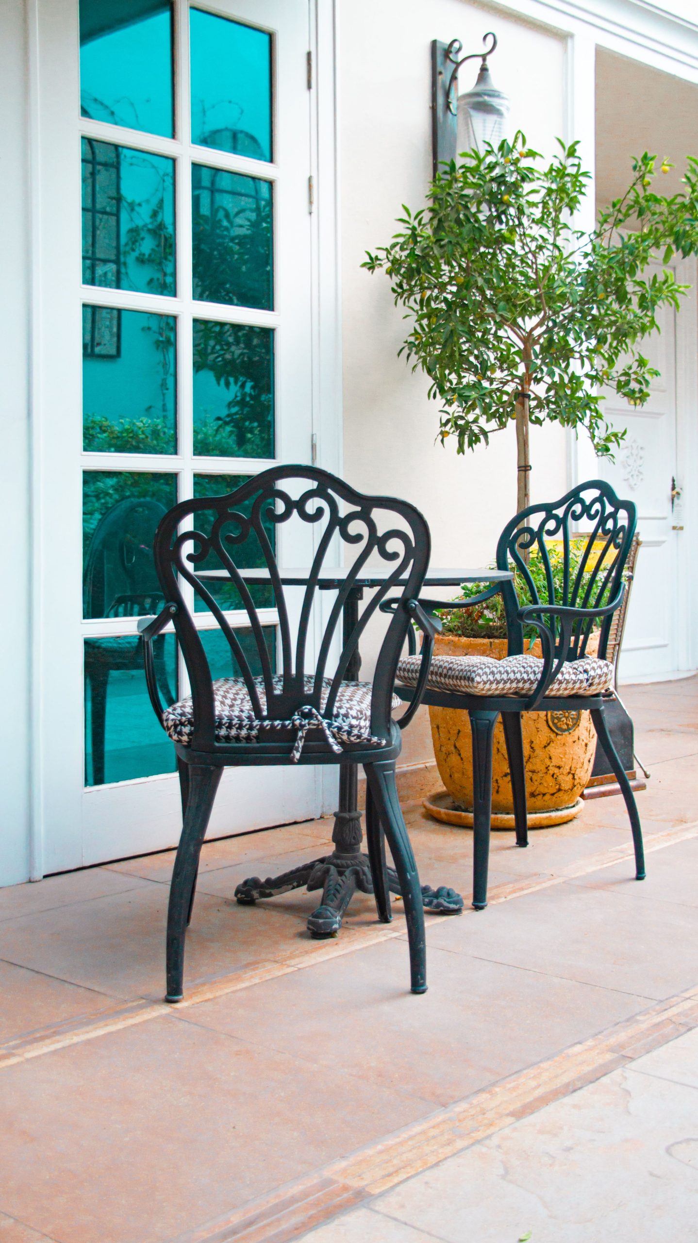 Elegant metal chairs on a sunny patio with decorative plants and a glass door.