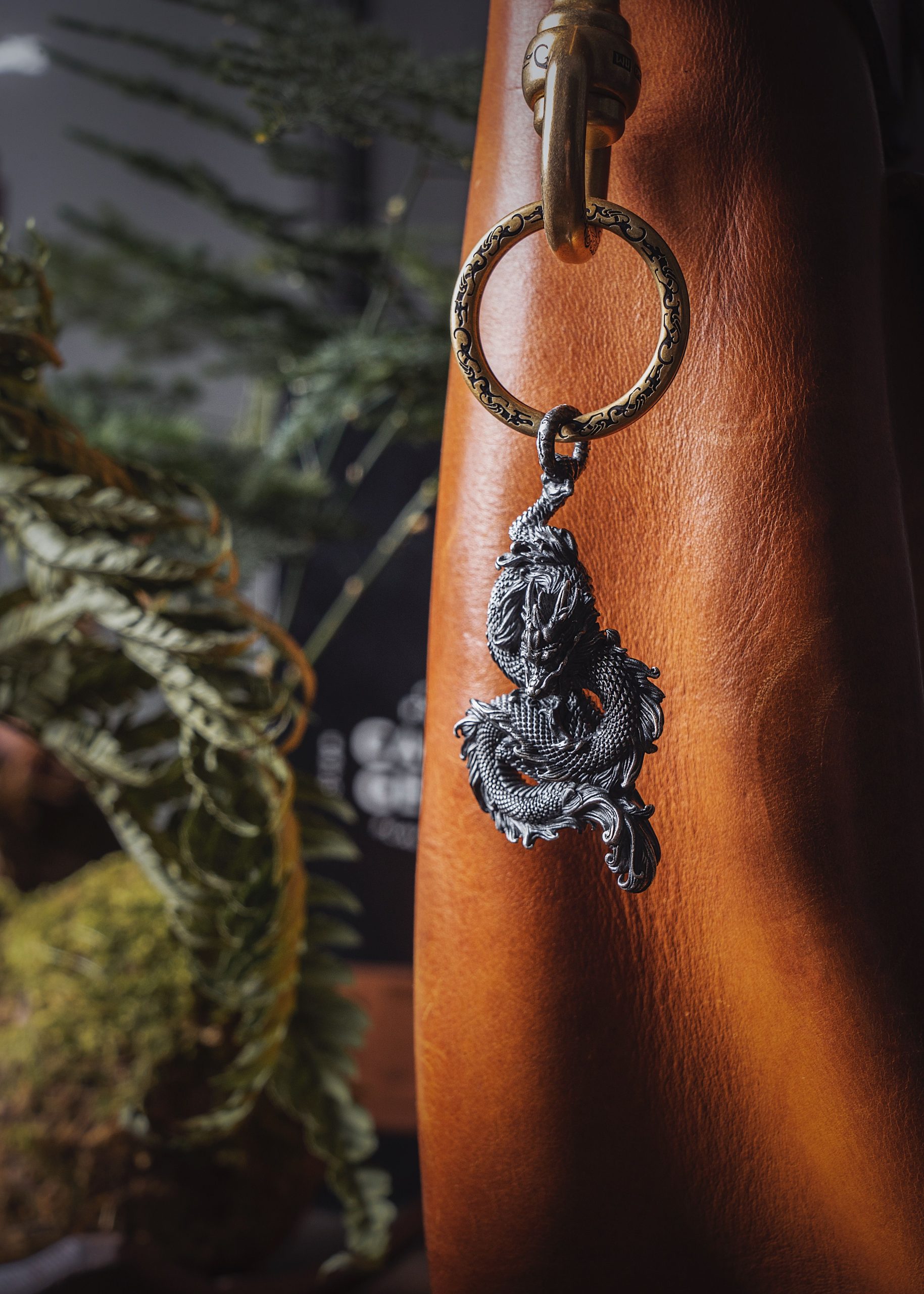 Elegant metal dragon keychain elegantly hangs from a leather bag, showcasing detailed craftsmanship in a classic setting.