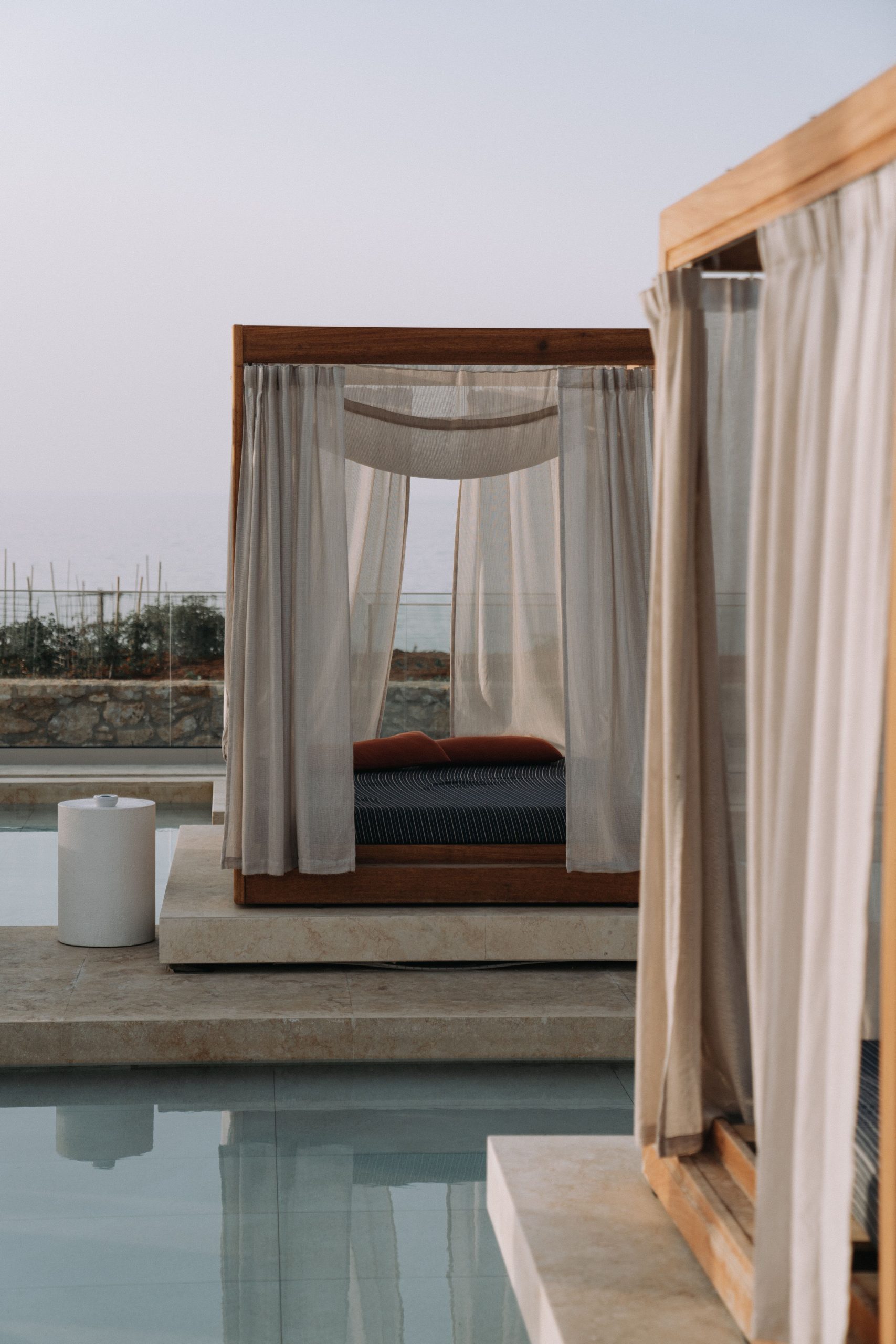 Elegant outdoor canopy bed by a serene poolside, offering luxury and relaxation.