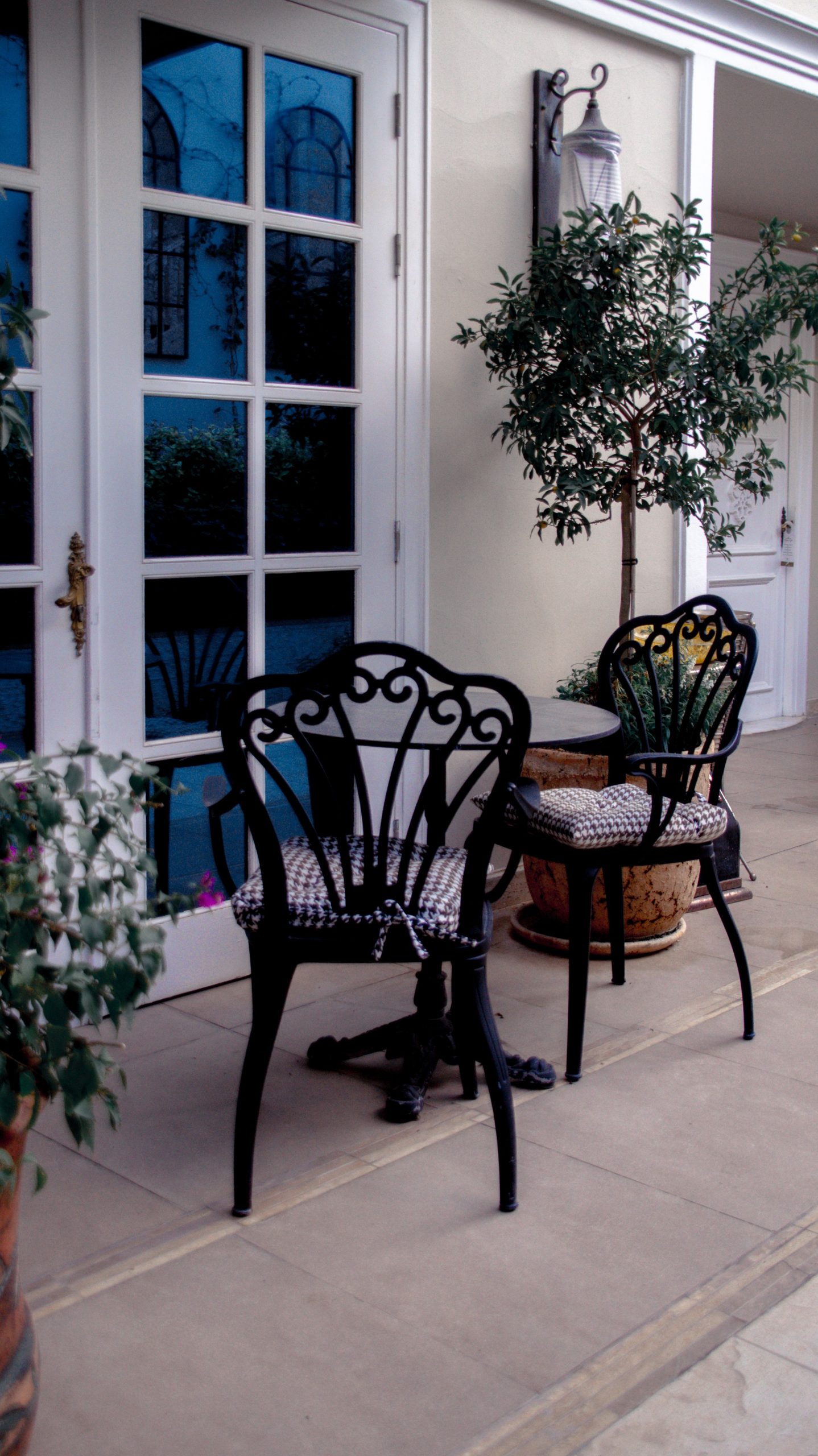 Elegant outdoor patio with vintage wrought iron chairs, potted plants, and decorative doorway.