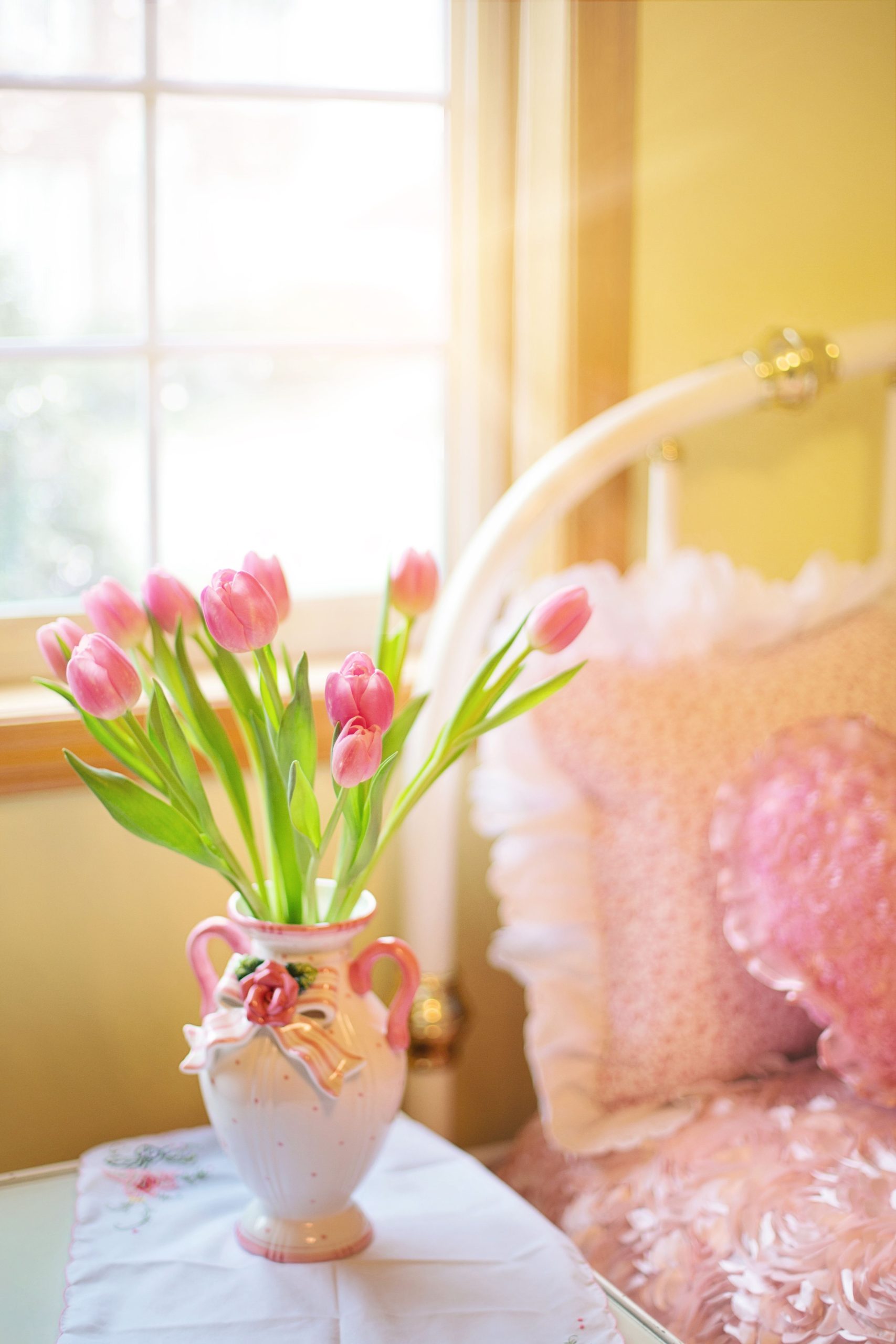 Elegant pink tulips in a vase with sunlight streaming through a window, adding a warm touch to the room.