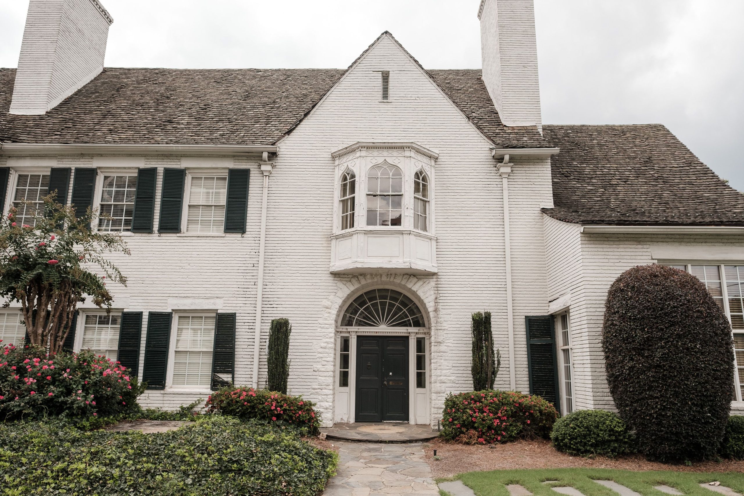Elegant white brick house with green shutters, lush garden, and a curved walkway accentuating its classic facade.