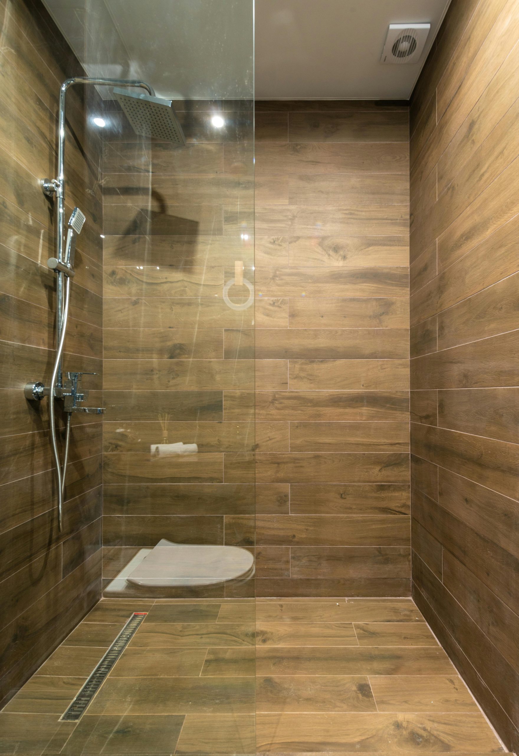 Elegant wooden-themed shower stall with clean glass partition in a modern bathroom setting.