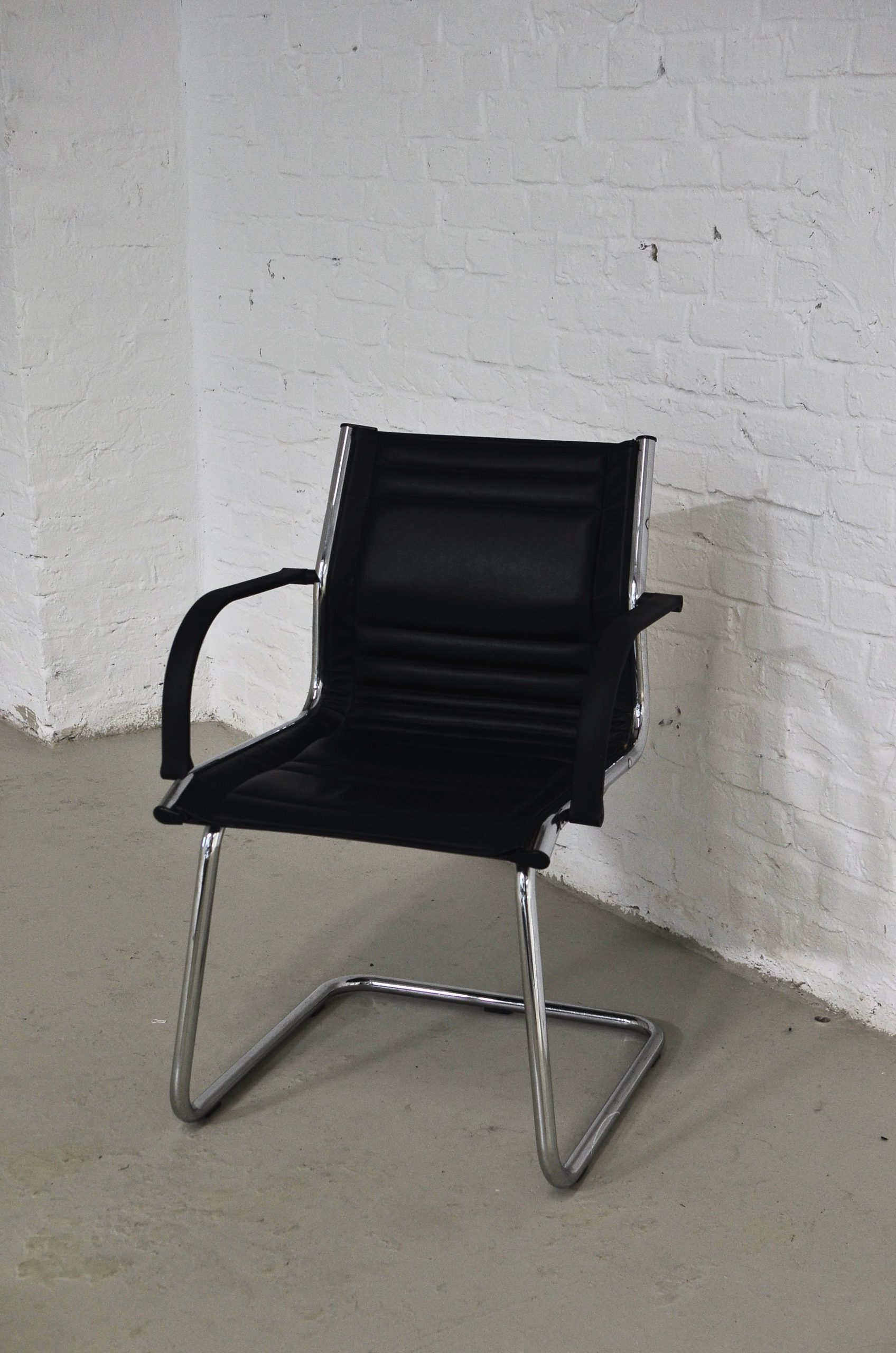 Empty black chair with metal elements placed in room against white brick wall