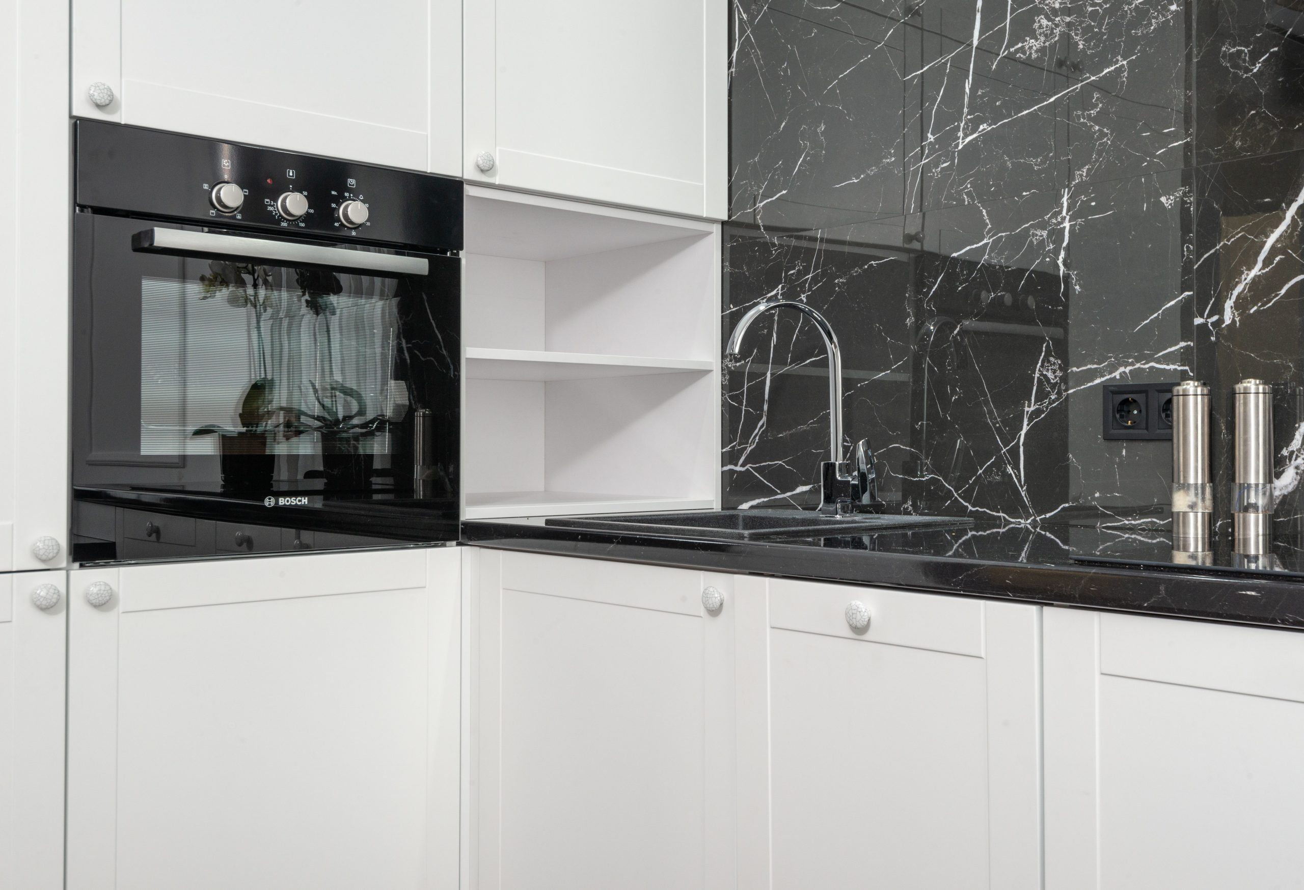Interior details of modern kitchen with white cabinets and black glossy marble backsplash and modern appliances in daylight