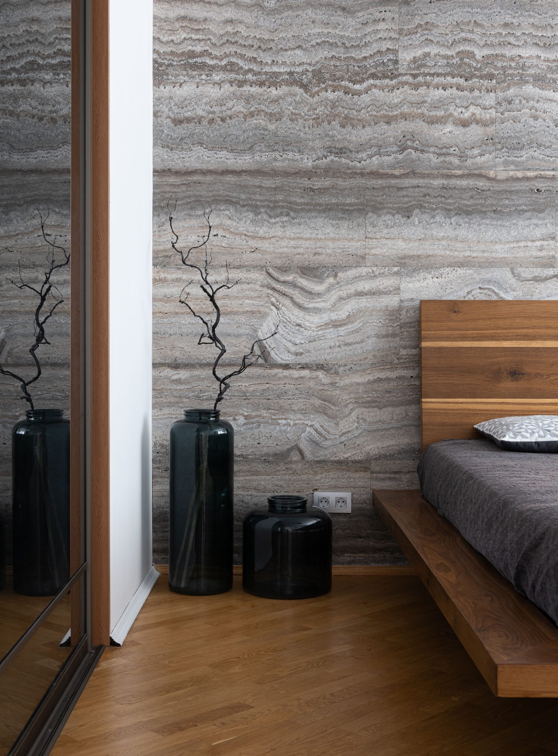 Interior of light modern flat with bed near vases with leafless sprig and mirror wall