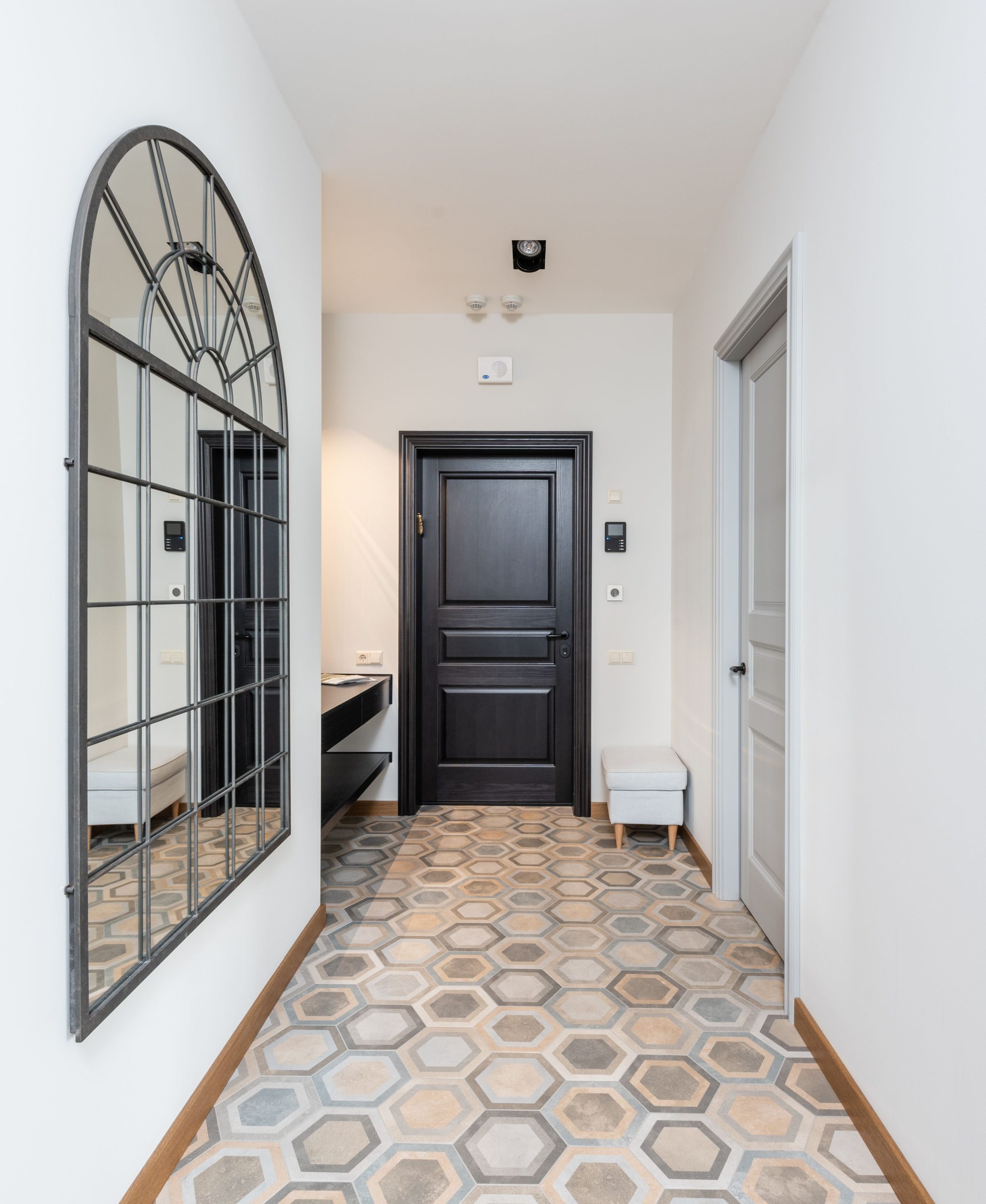 Interior of spacious corridor with colorful tile floor and decorative mirror hanging on light wall placed in contemporary apartment