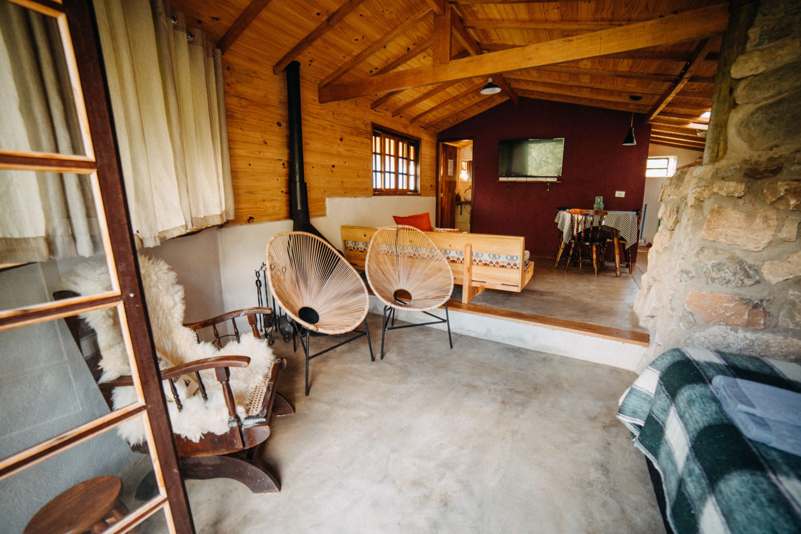 Interior of spacious cottage with table and armchairs placed near bed in rustic style house with wooden walls located in countryside