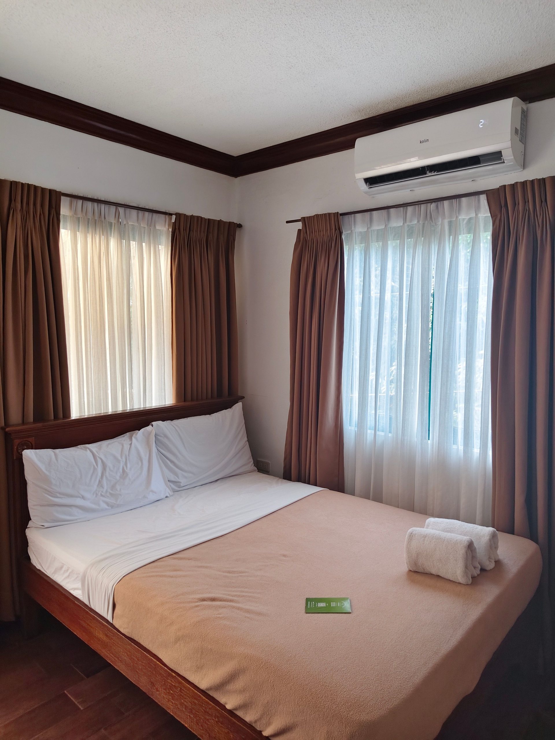 Inviting bedroom with natural light, featuring a bed, curtains, and an air conditioner.