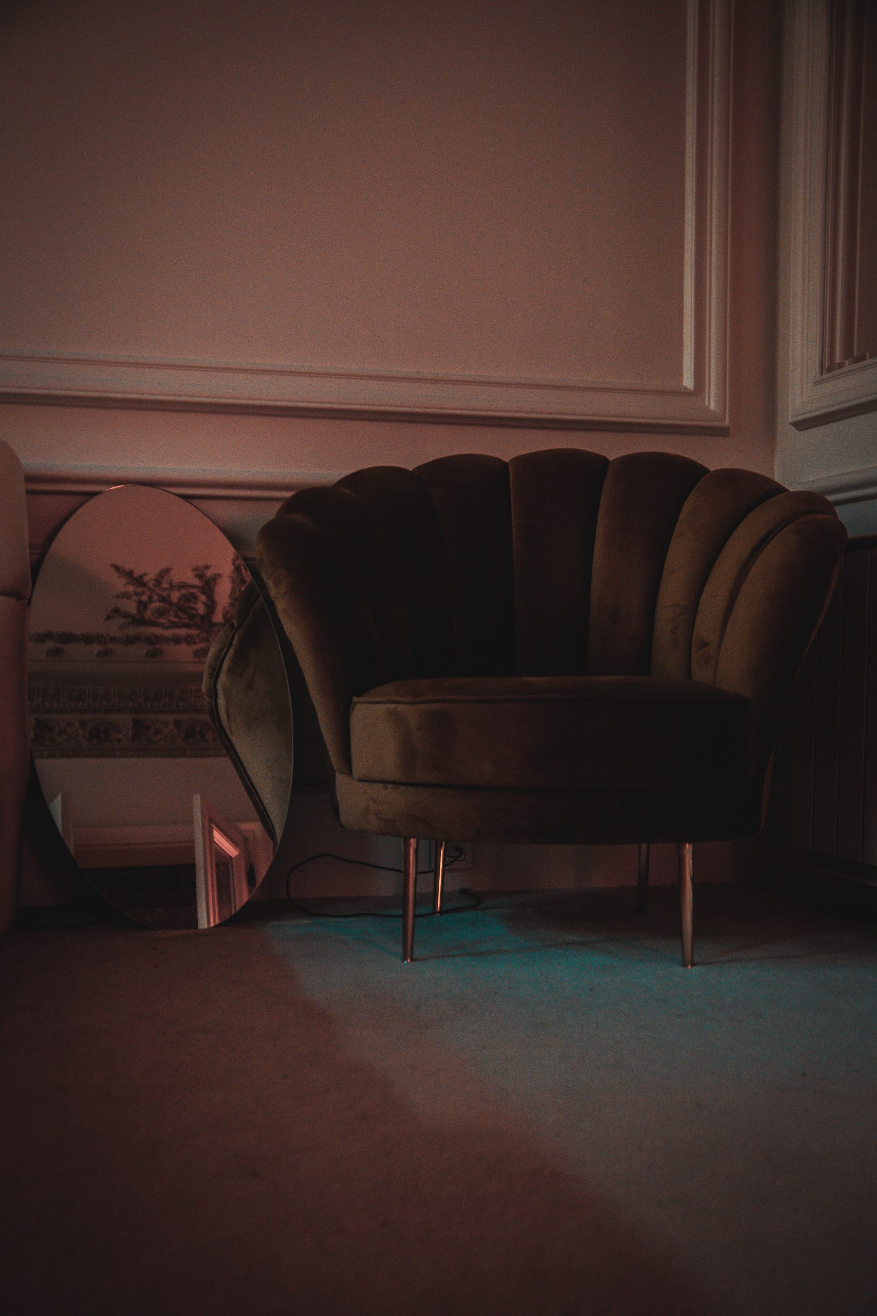Luxurious velvet chair beside an oval mirror in a softly lit, stylish interior.
