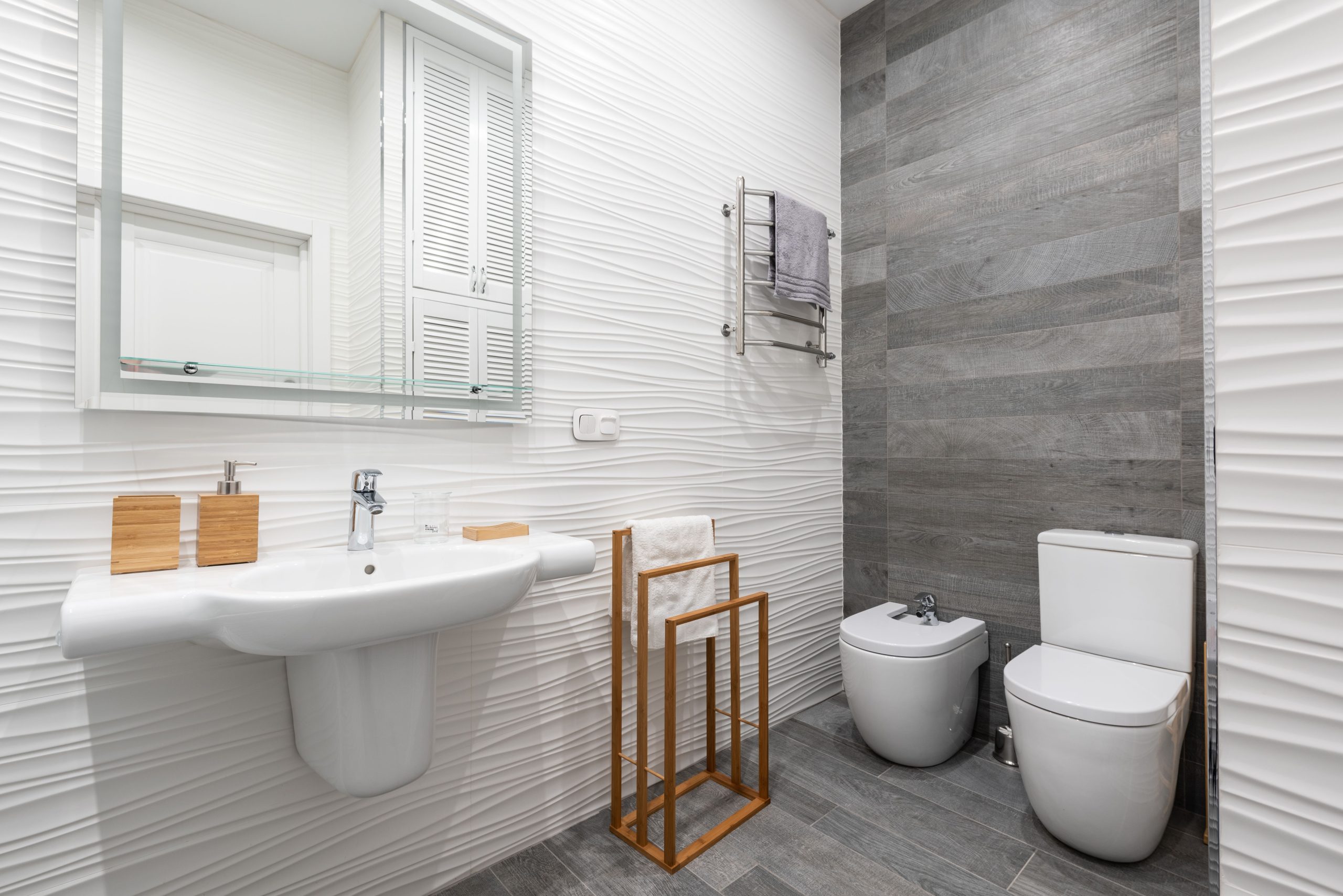 Modern bathroom with washstand under mirror and bidet on ceramic floor with towel on rack at home