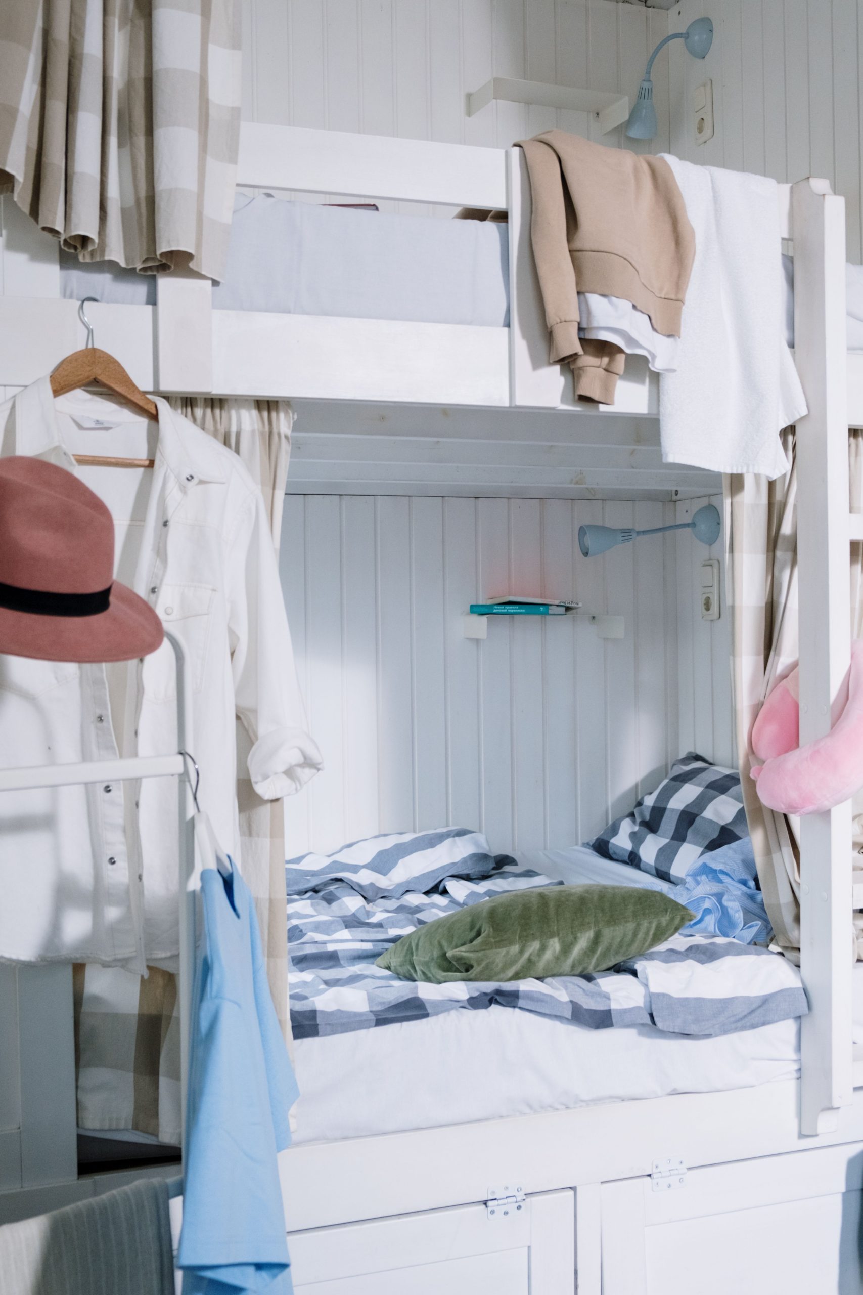 Neatly arranged dorm room featuring a stylish bunk bed with hanging clothes and vibrant decor.