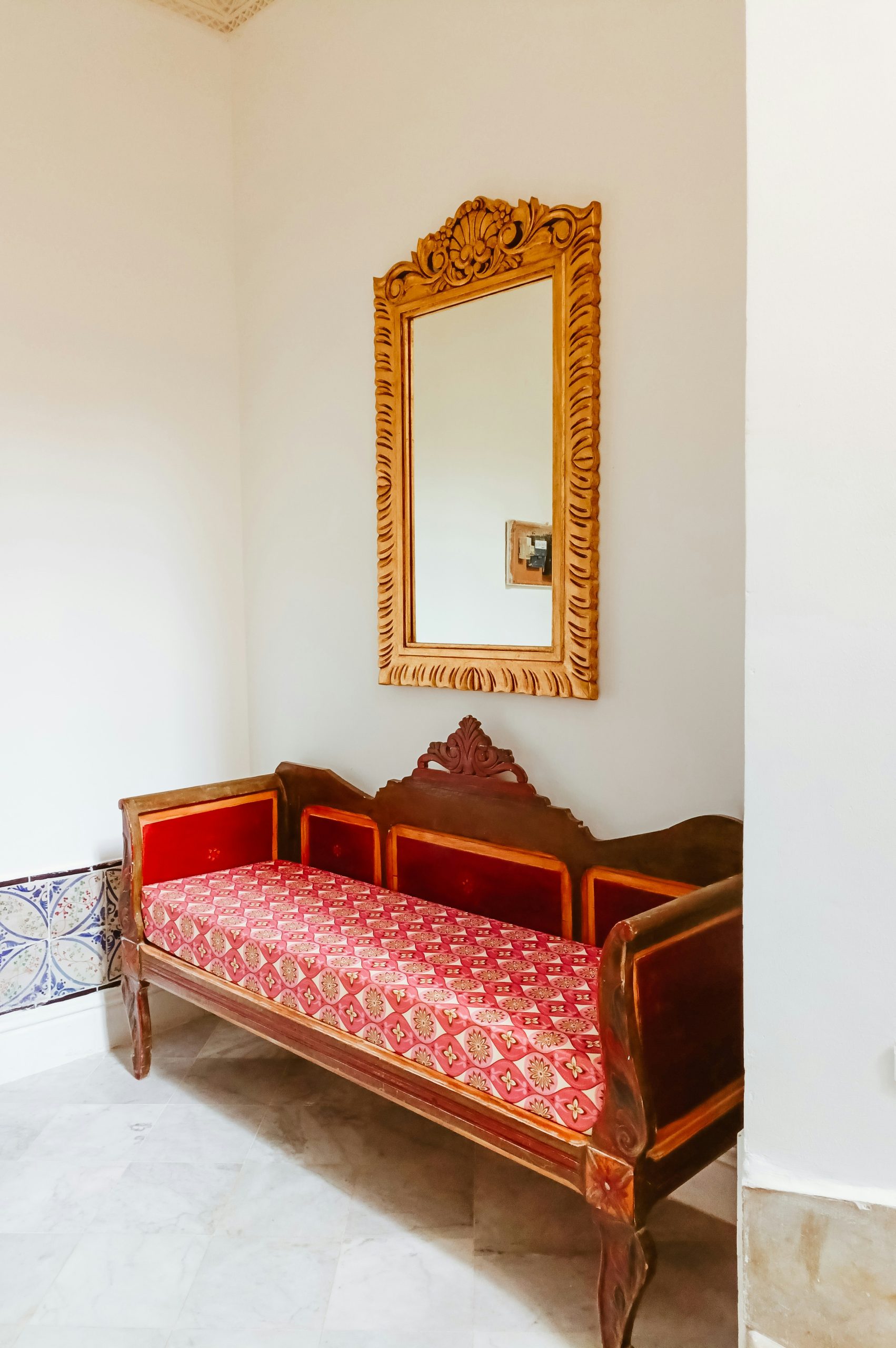 Ornate golden mirror above a vintage red wooden sofa.
