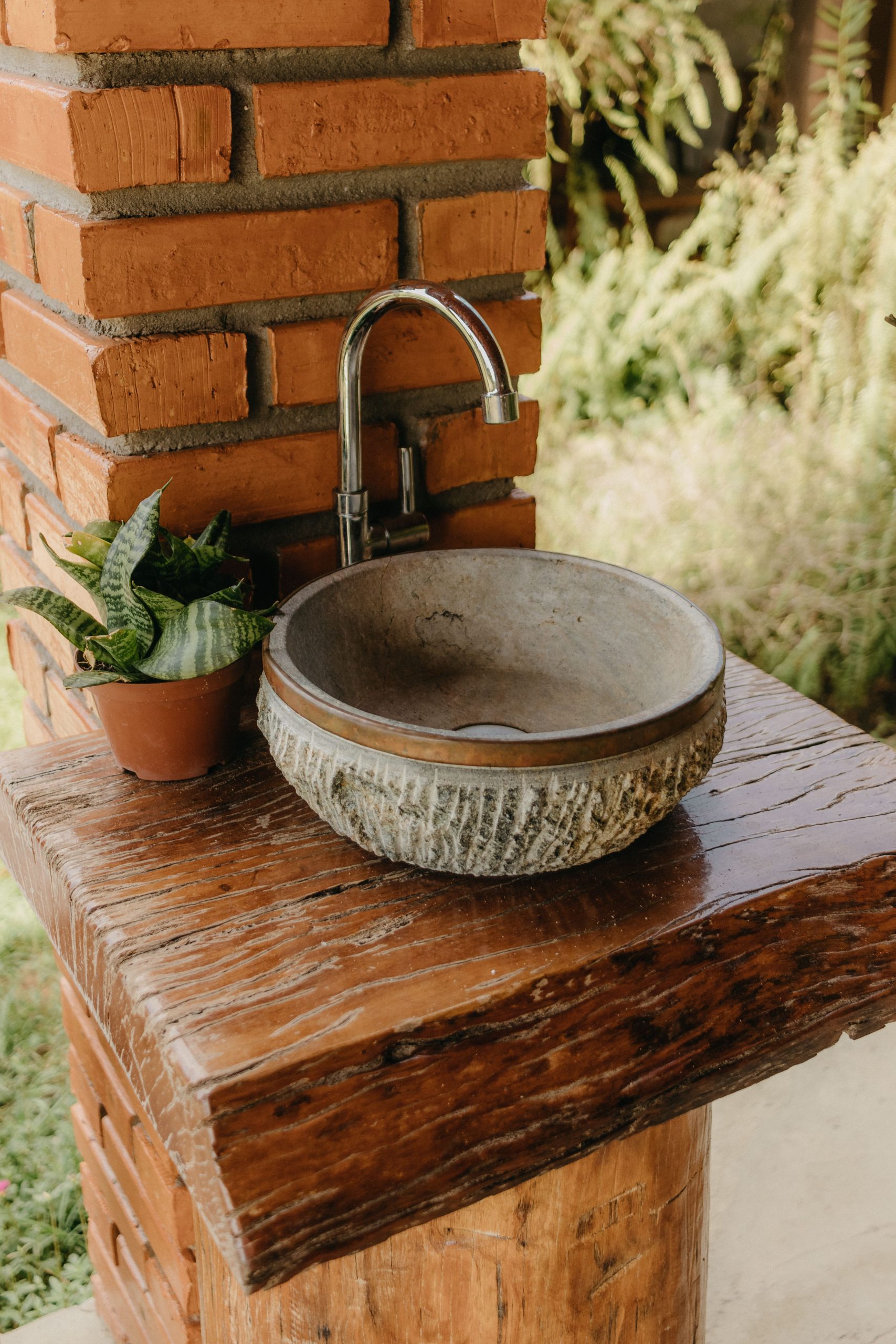 Outdoor rustic stone sink with wooden pedestal and potted plant for a natural look.