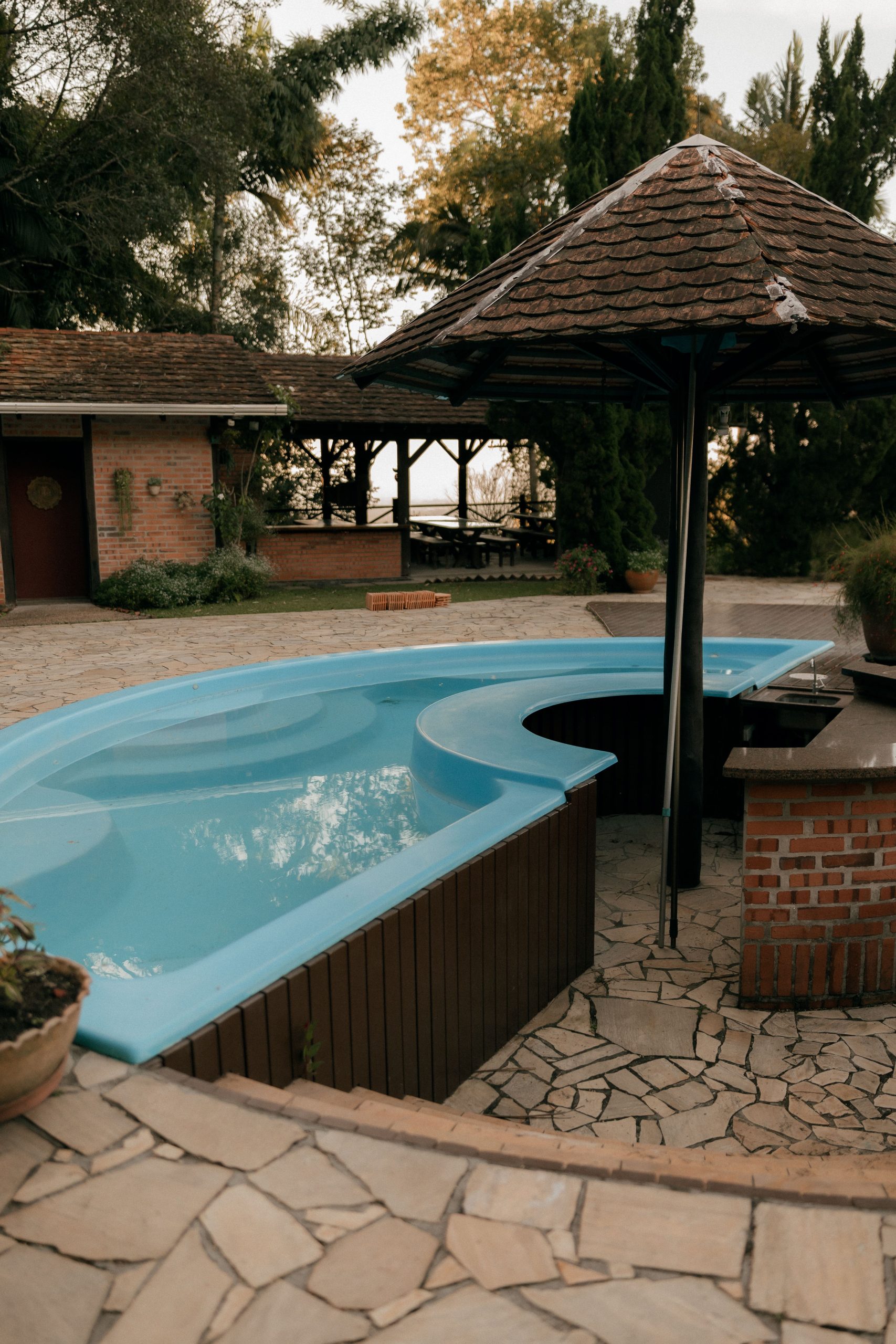 Rustic outdoor patio with curvy pool, brick gazebo, and lush greenery, perfect for relaxation.