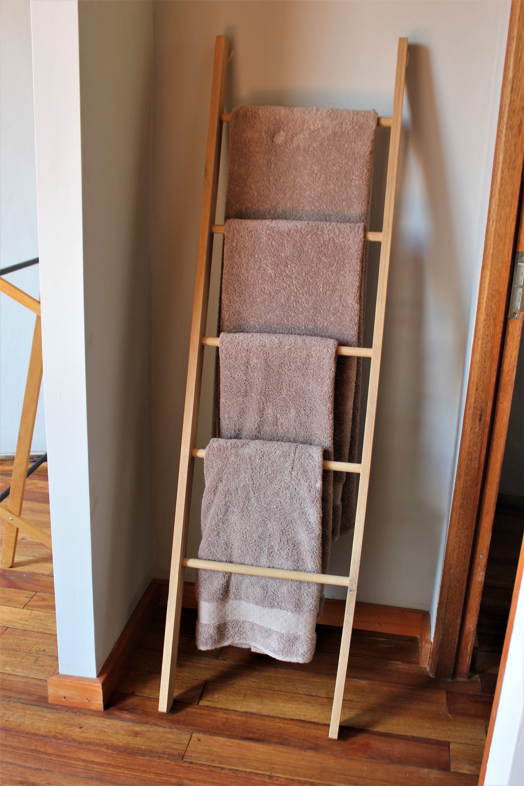 Simple wooden towel rack with neatly hung towels in a modern, minimalist home setting.