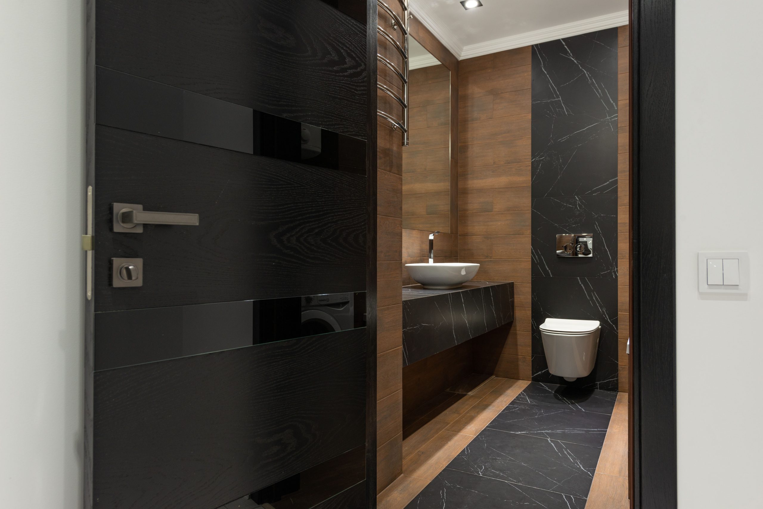 Sleek bathroom with black marble tiles and wooden accents, featuring a modern sink and toilet.