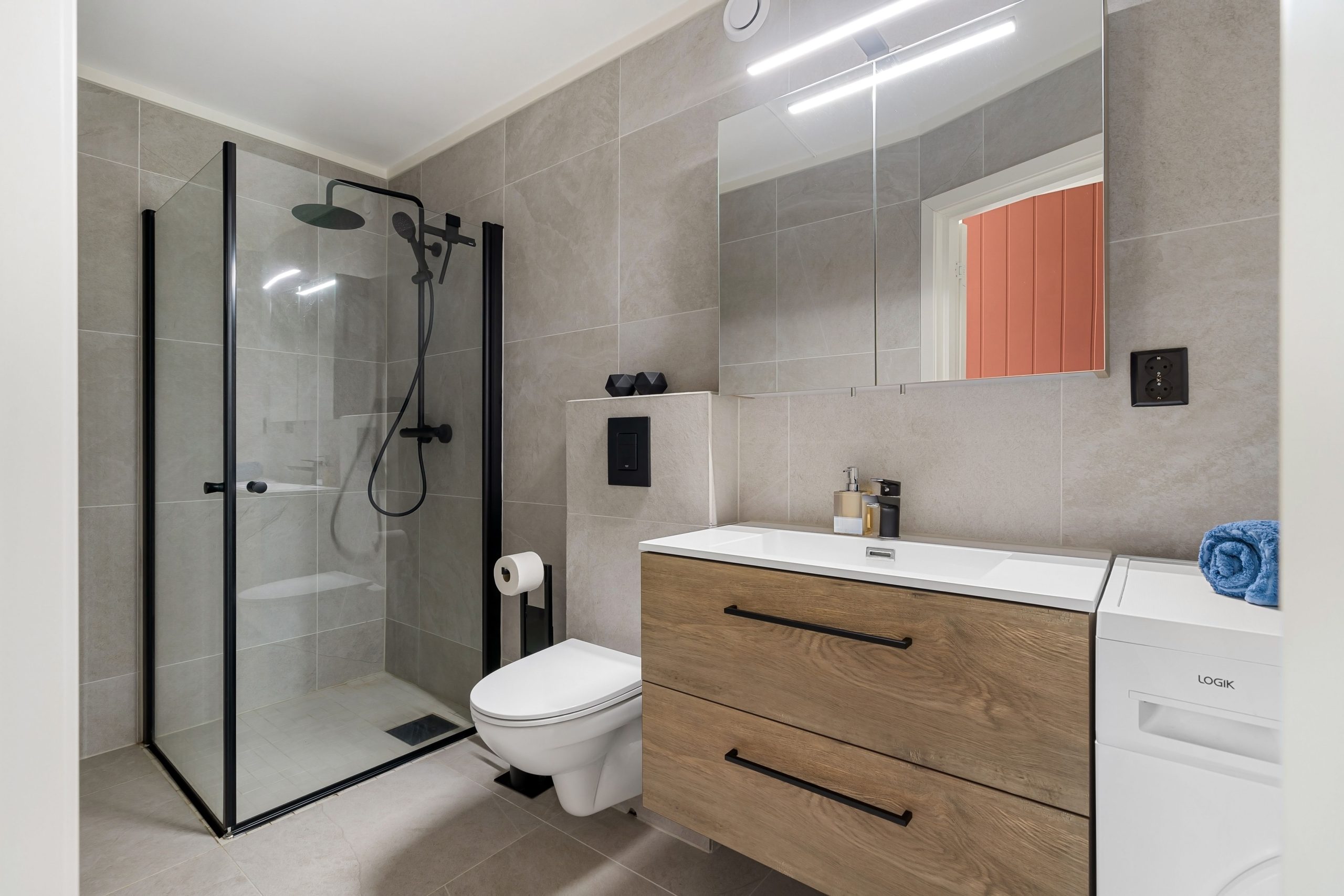 Sleek contemporary bathroom with glass shower, wood vanity, and washing machine.