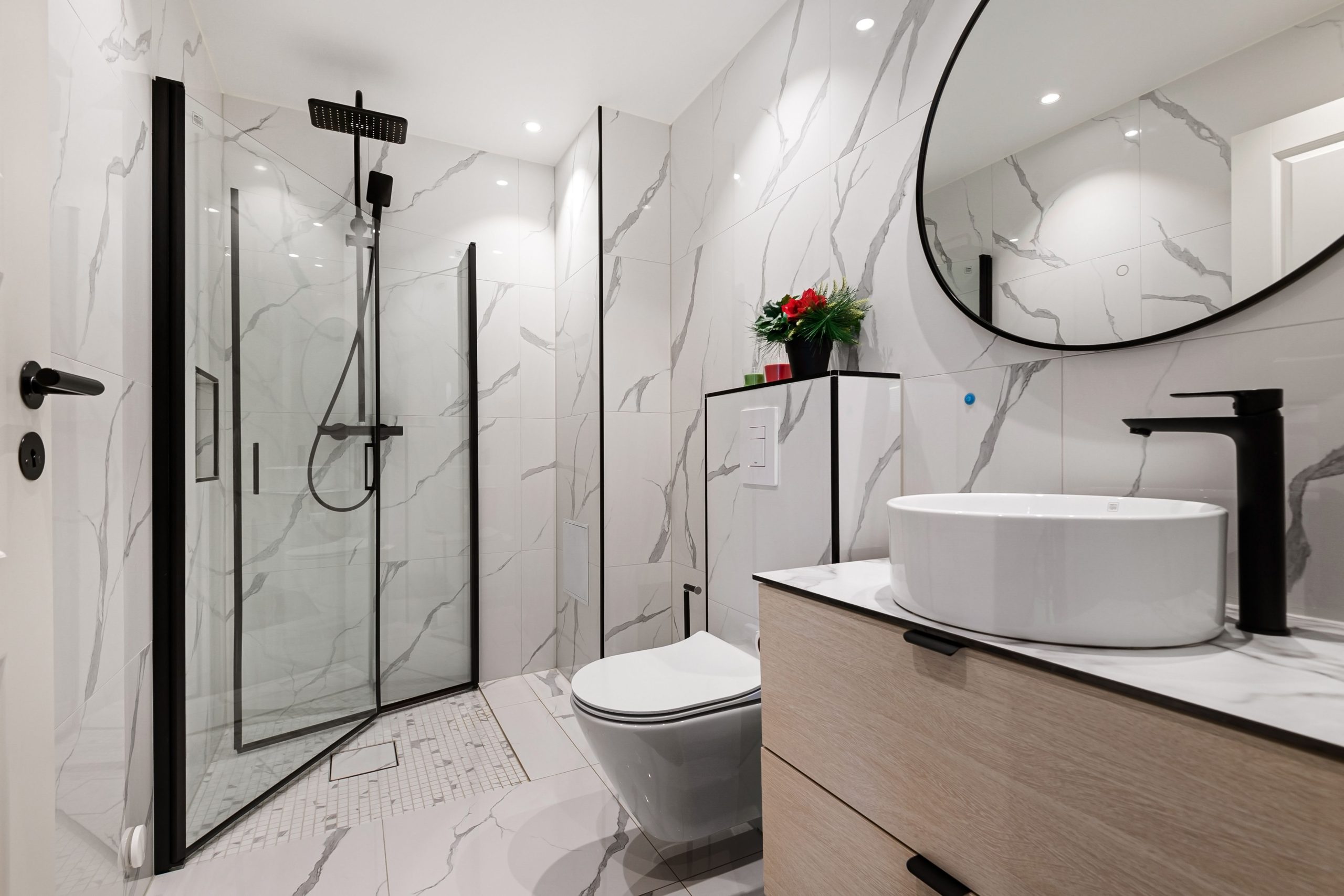 Sleek minimalist bathroom featuring marble walls, black fixtures, and a round mirror.