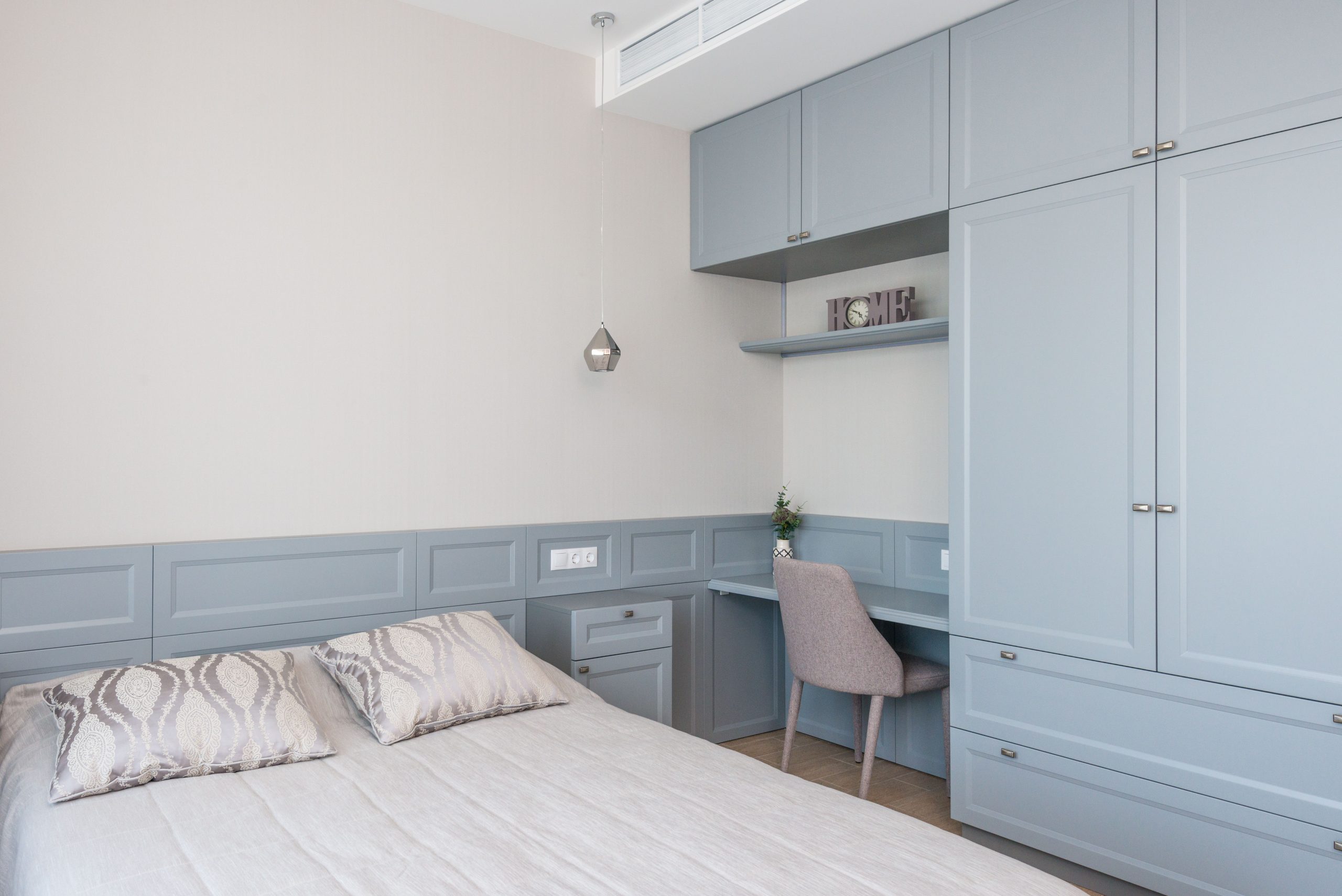 Stylish bedroom features built-in cabinetry, soft blue tones, and a cozy workspace.