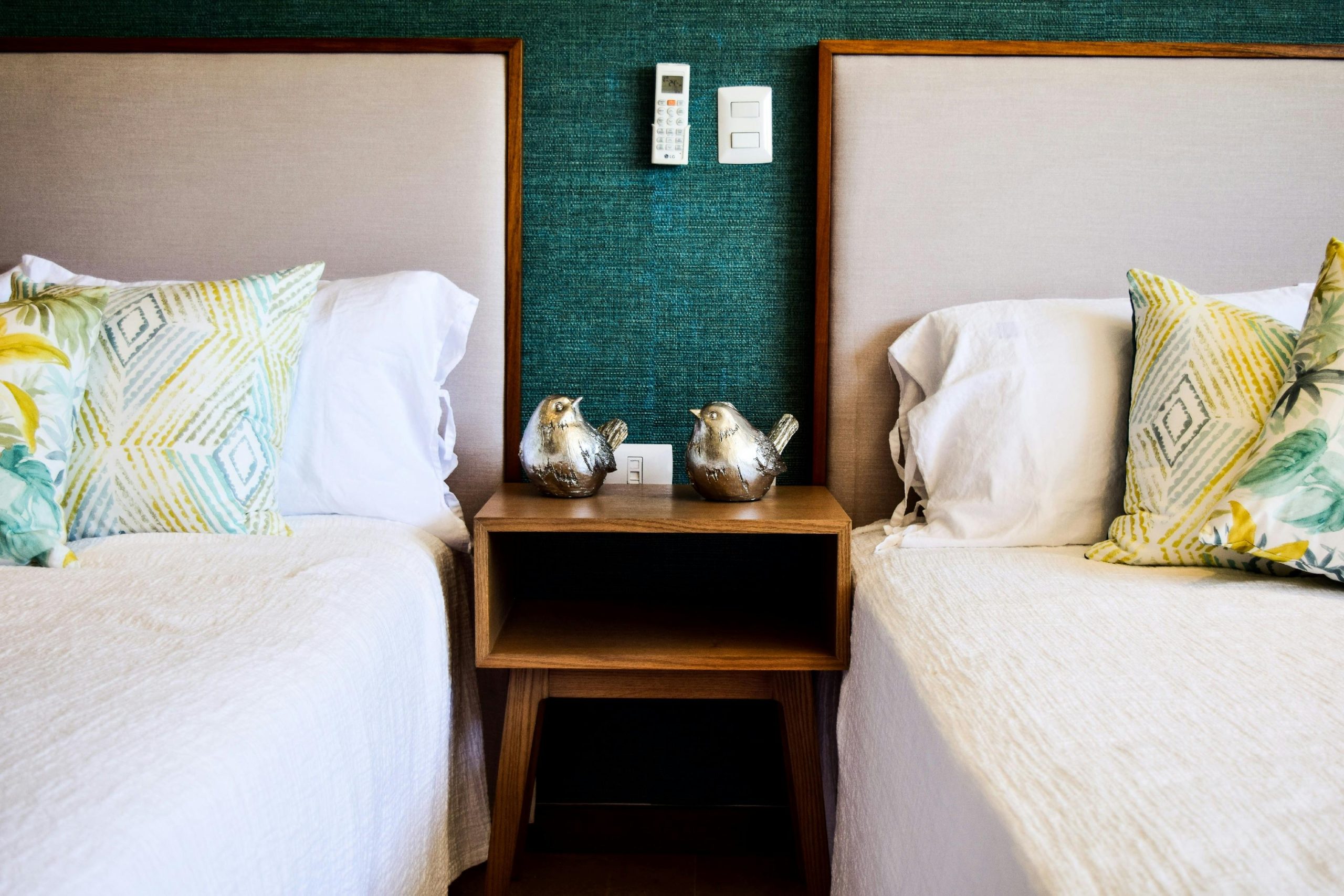 Stylish bedroom setting with twin beds, decorative pillows, and silver bird figurines on a wooden nightstand.