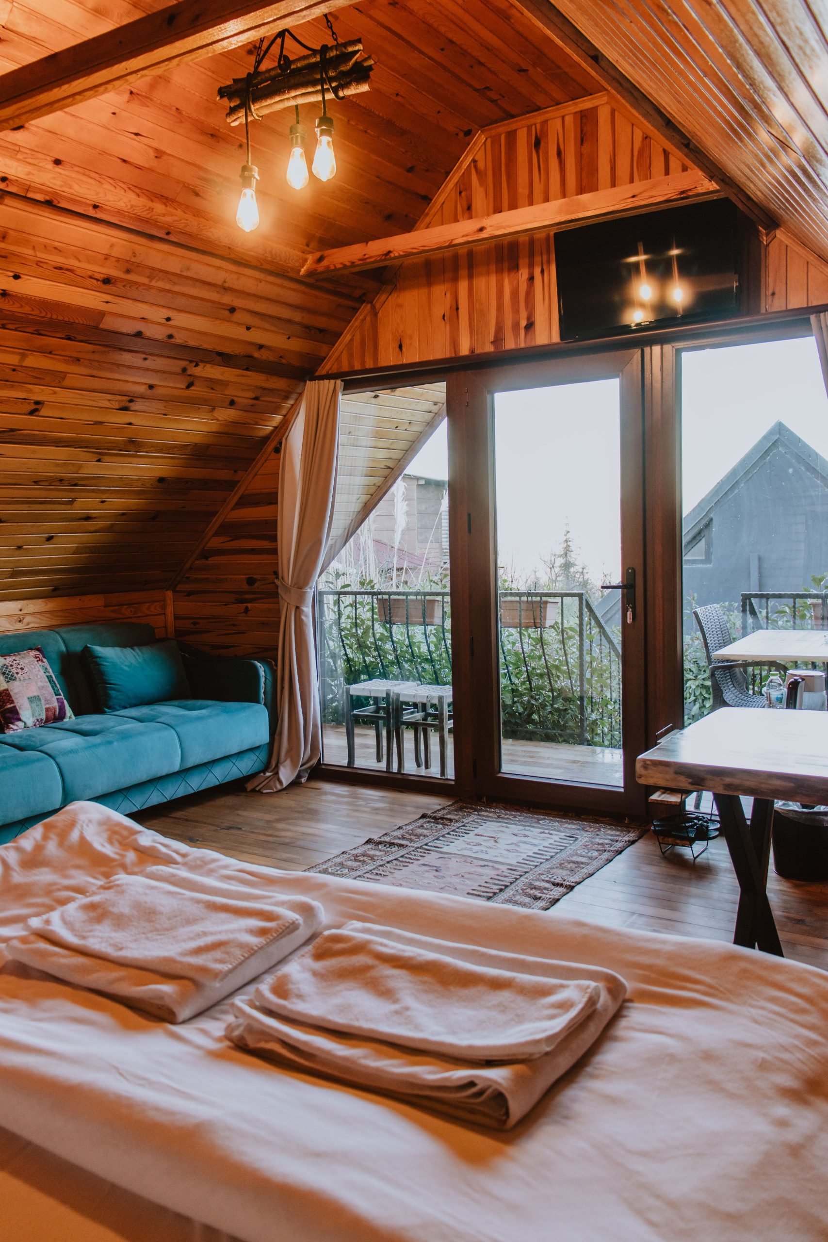 Warm attic bedroom interior with wooden decor and glass doors opening to a scenic view.