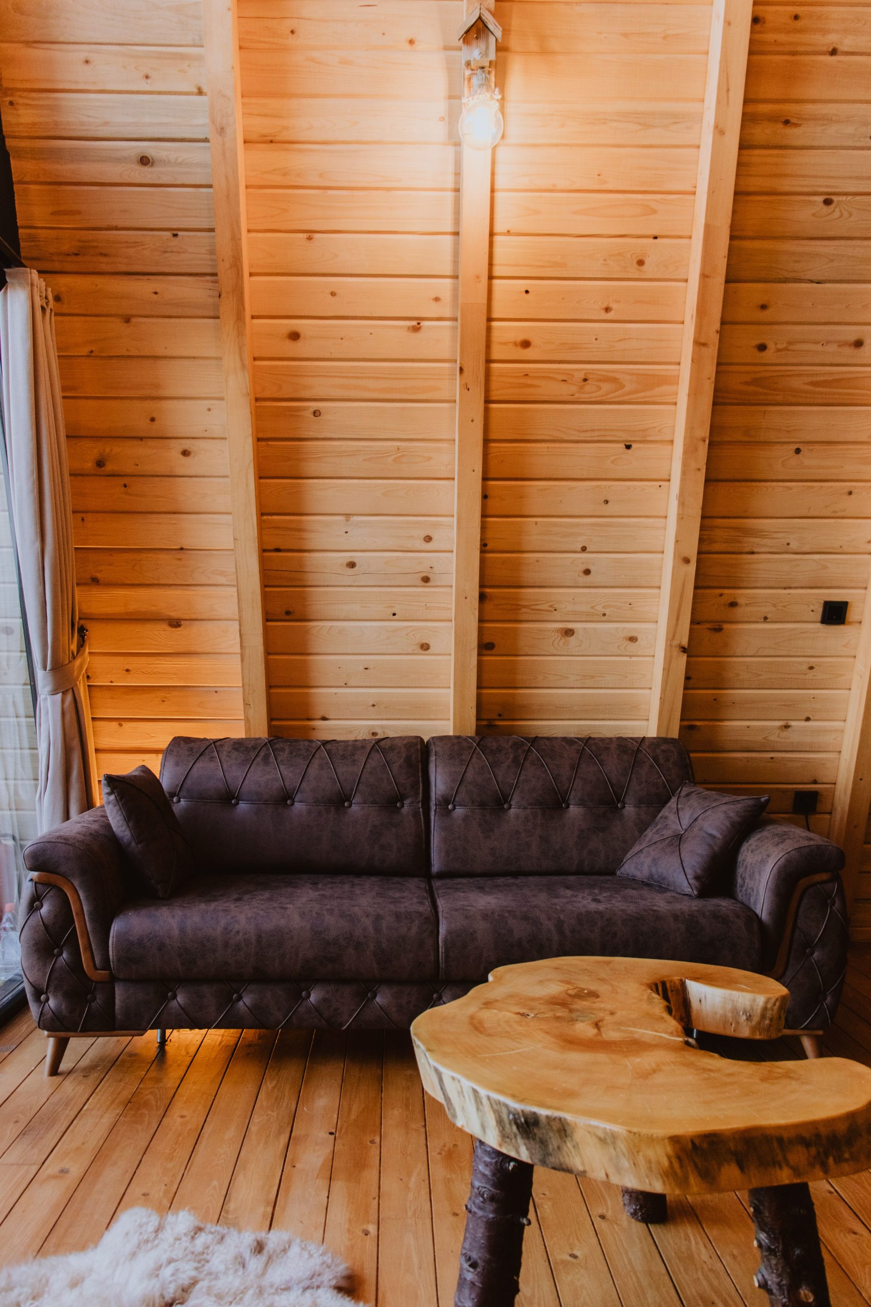 Warm wooden interior featuring a cozy sofa and uniquely shaped wooden table, perfect for relaxation.