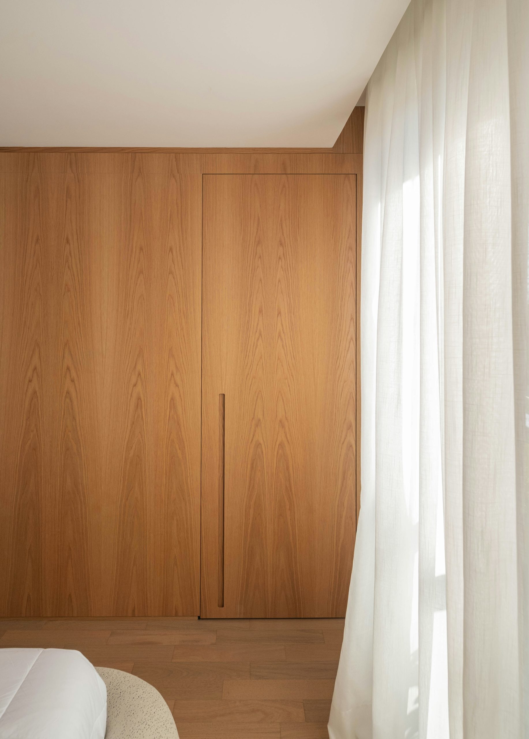 Wooden closet beside a sheer curtained window.