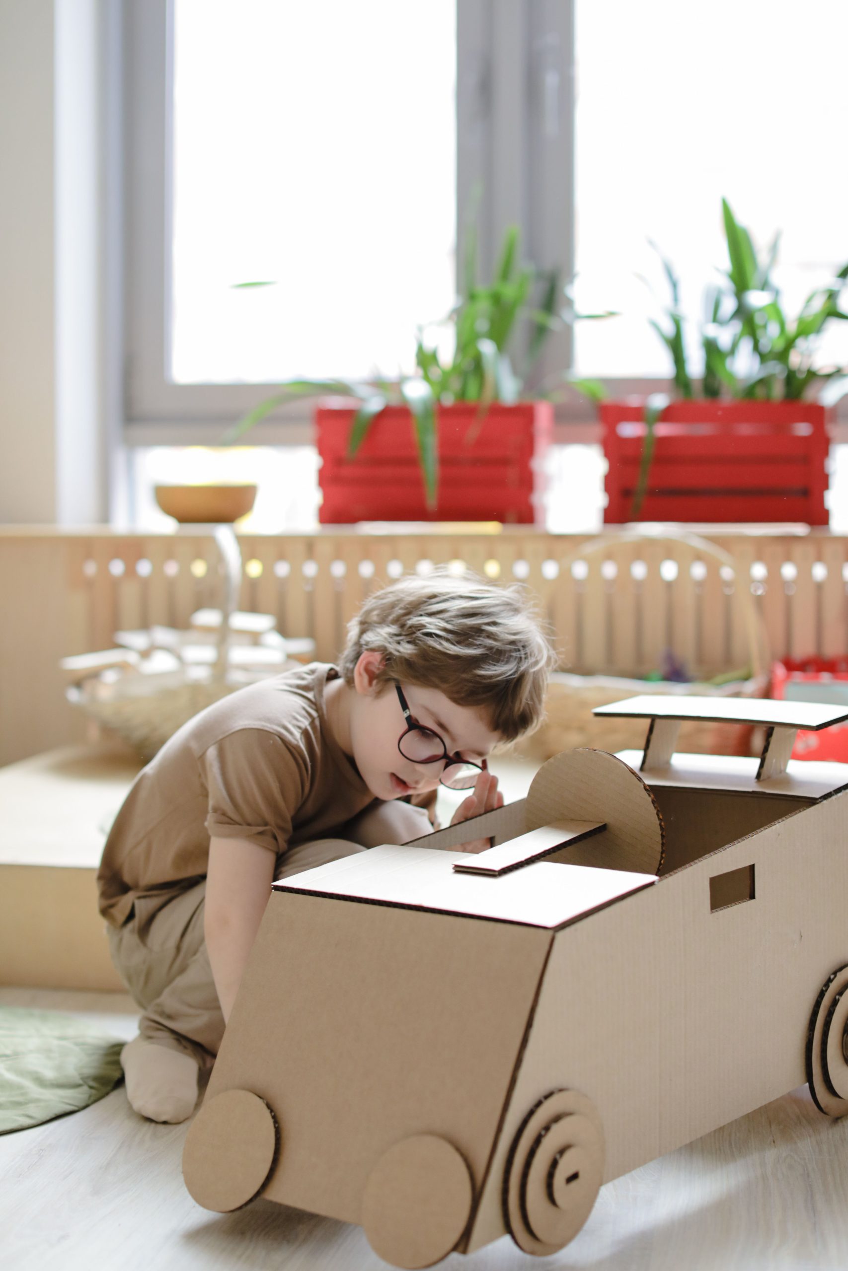 Young boy engaged in creative play with a cardboard car in a cozy indoor setting.