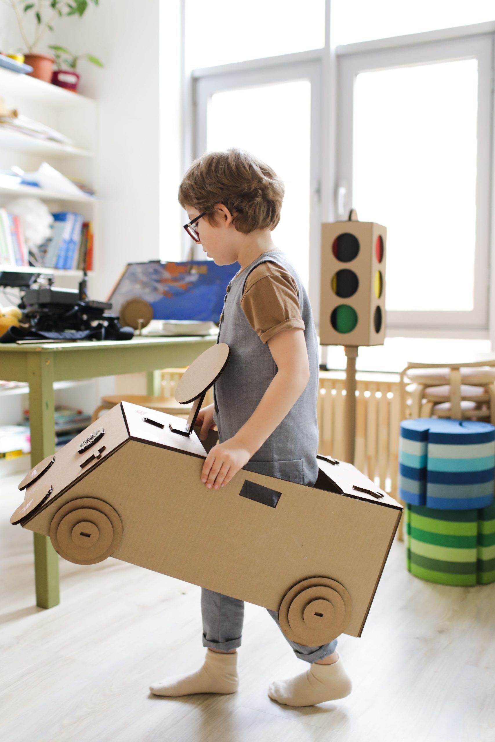 Young child engaged in imaginative play with handmade cardboard car in educational setting.