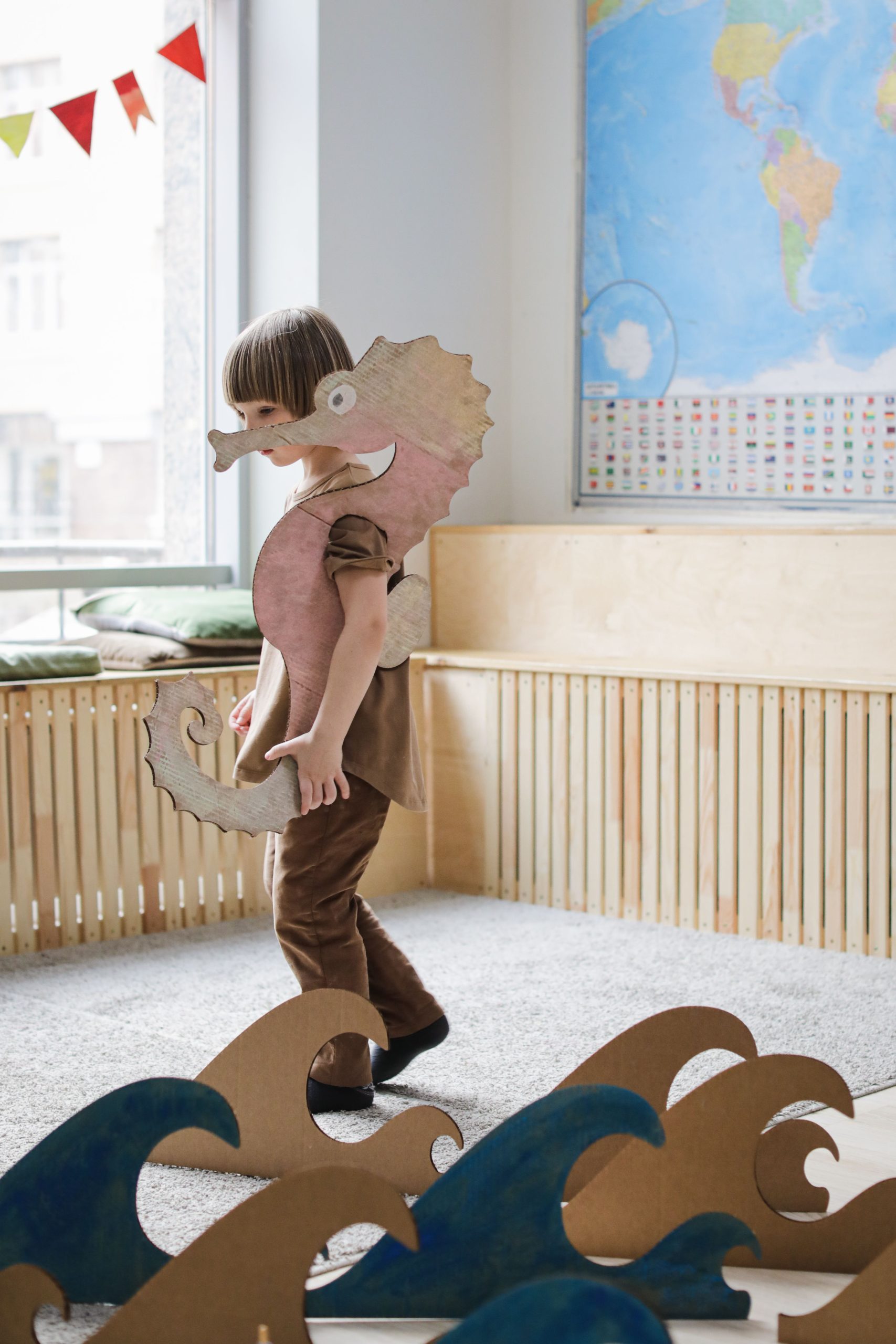 Young child wearing cardboard seahorse costume, plays creatively indoors.