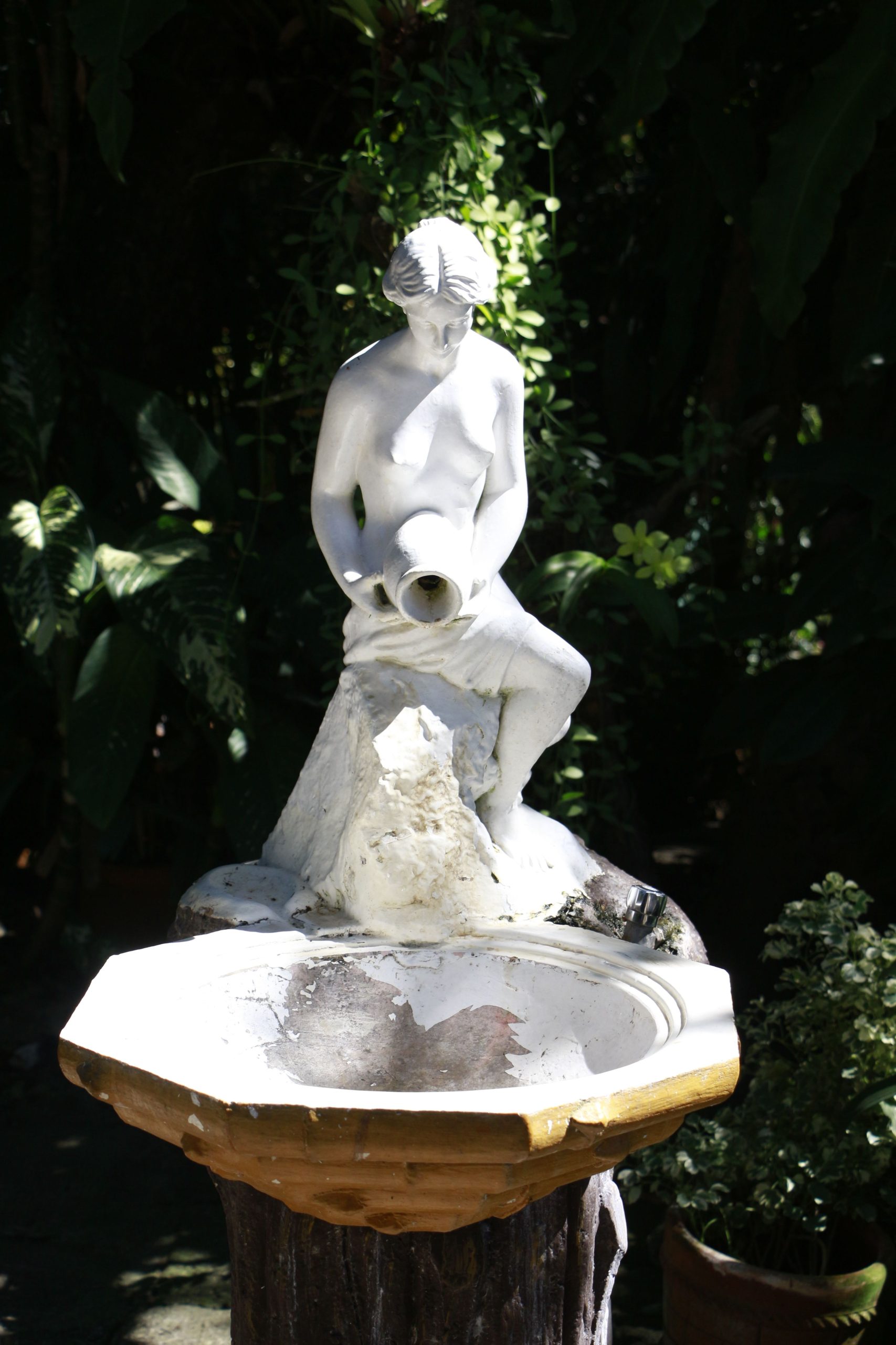 A beautiful marble fountain with a classical figurative statue in a lush garden setting.