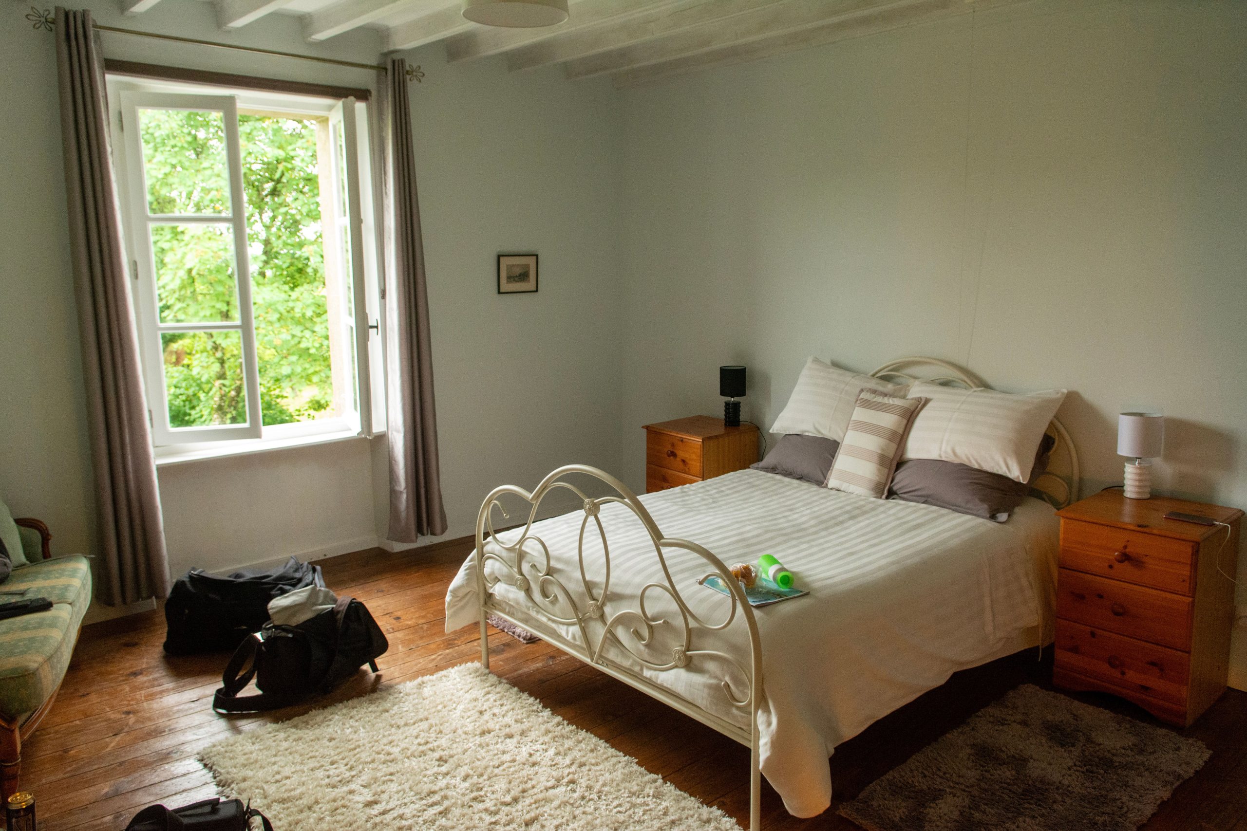 A bright and inviting bedroom with vintage furniture and a view of lush greenery through a large window.