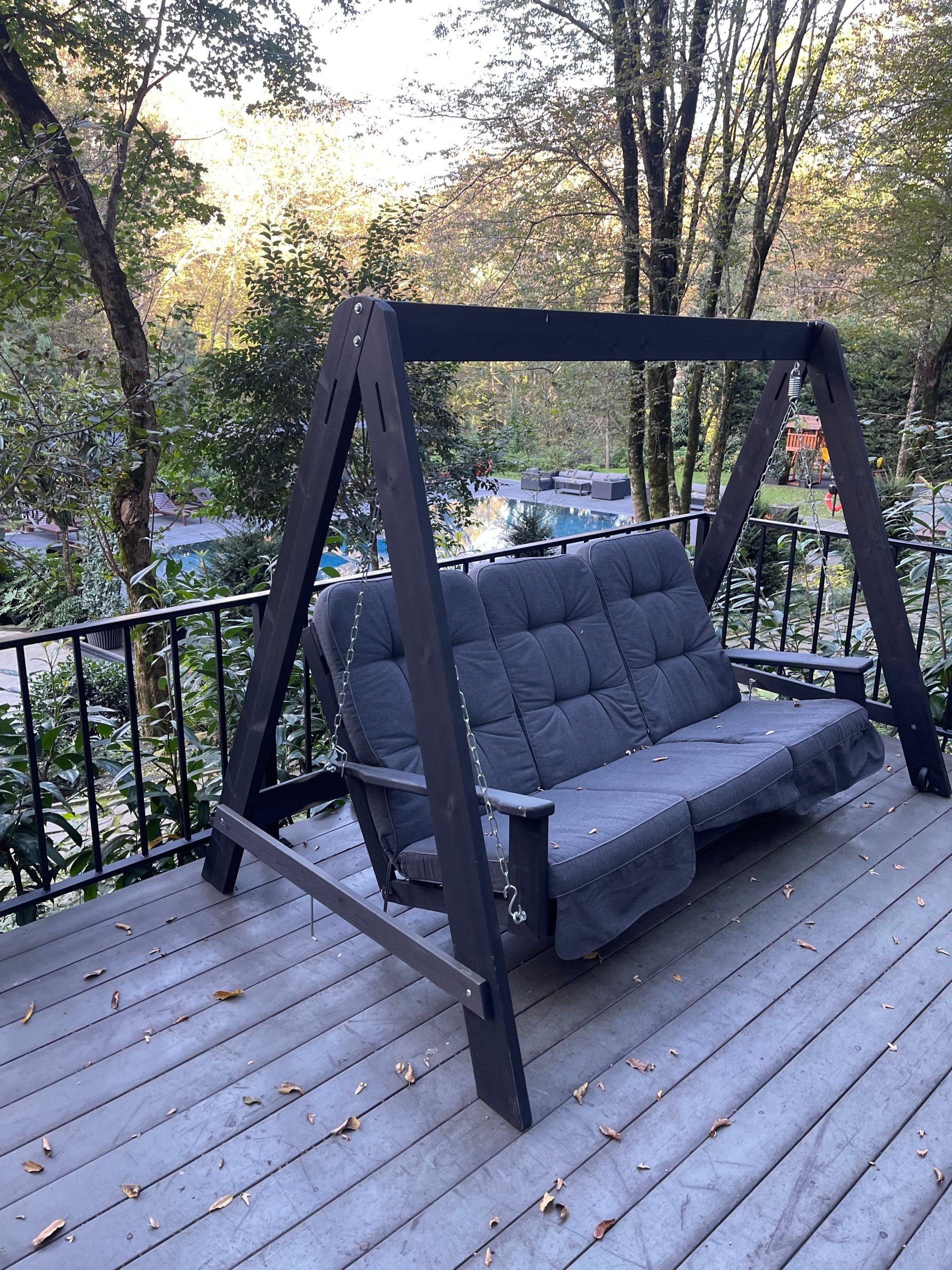 A comfortable outdoor swing surrounded by lush forest, perfect for relaxation on a wooden deck.