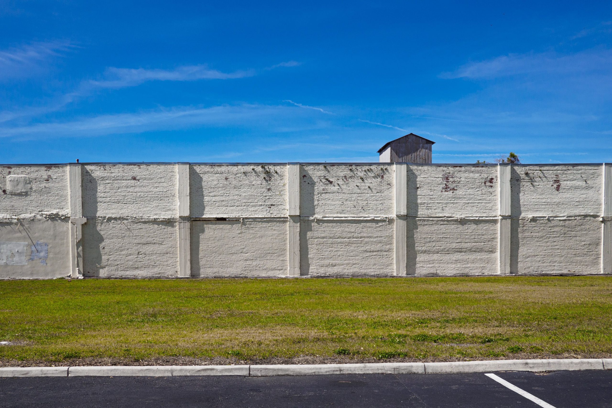 A concrete wall under a clear blue sky with green grass in an urban setting.