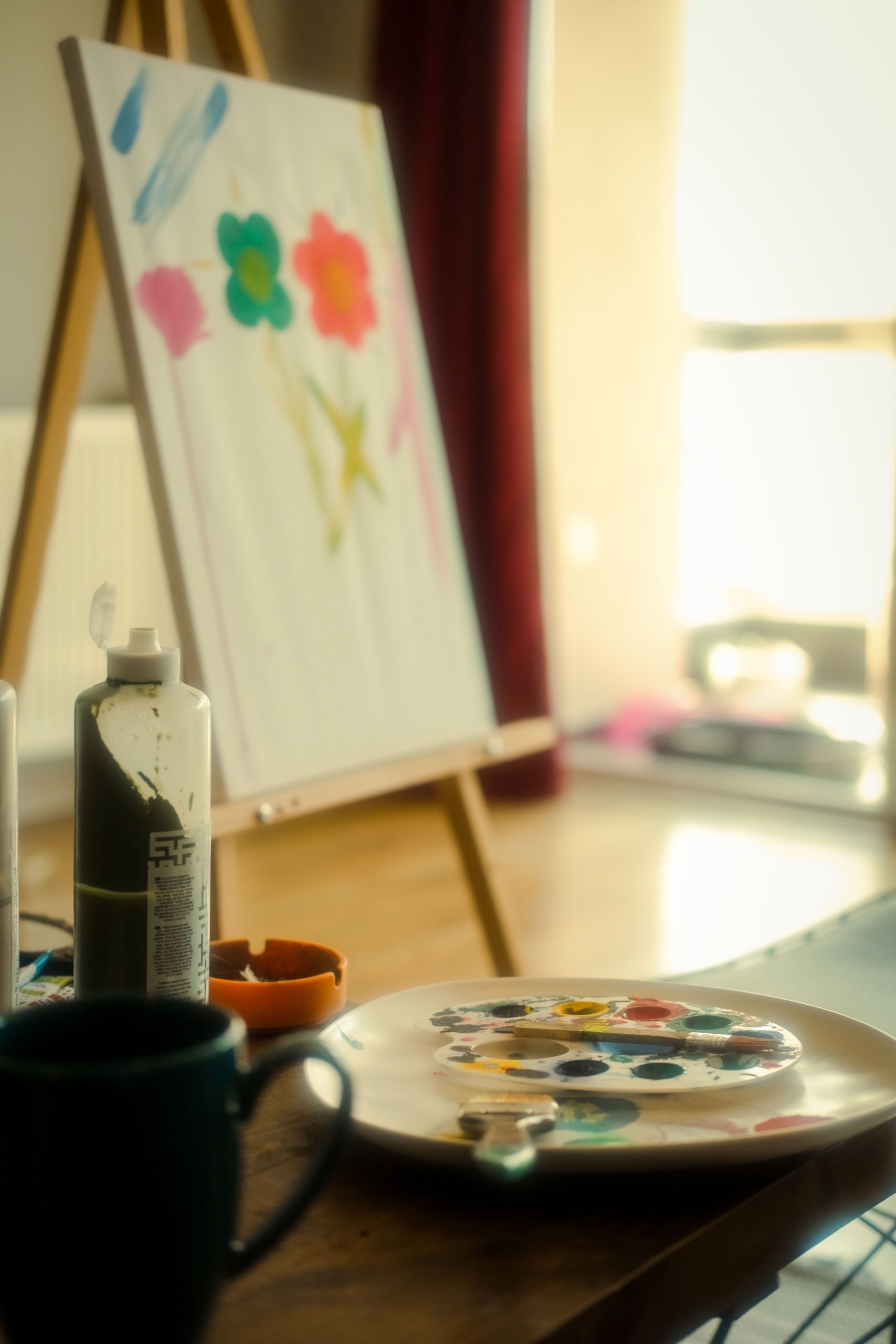 A cozy art studio with a canvas on an easel, surrounded by painting supplies, bathed in warm light.