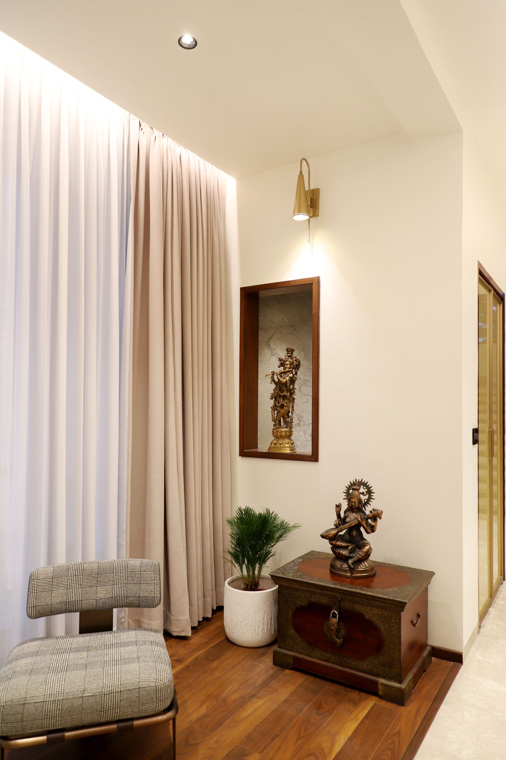 A cozy interior corner featuring a stylish chair, decor chest, and a statue under warm lighting.