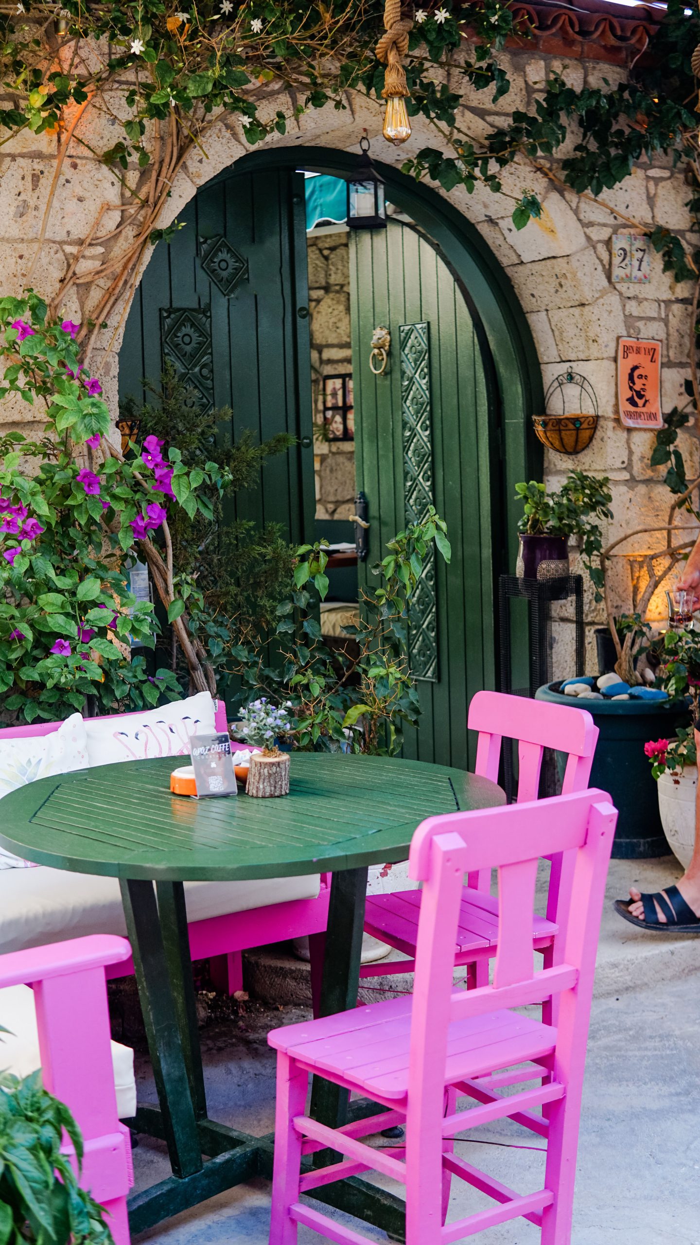 A cozy outdoor patio with colorful chairs and a rustic green door, surrounded by lush greenery.