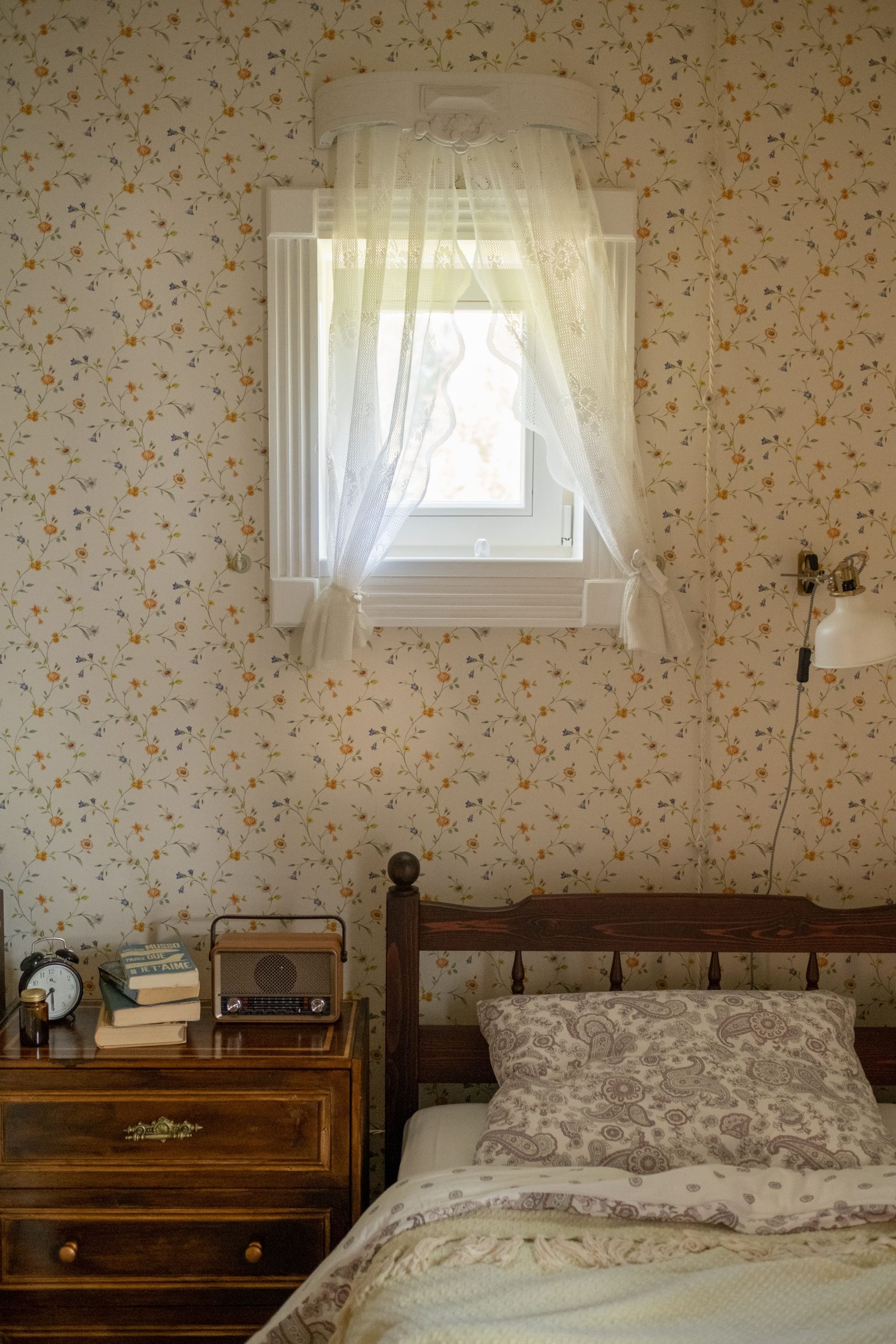 A cozy, vintage-style bedroom featuring a floral wallpaper, wooden bed, and nostalgic decor.