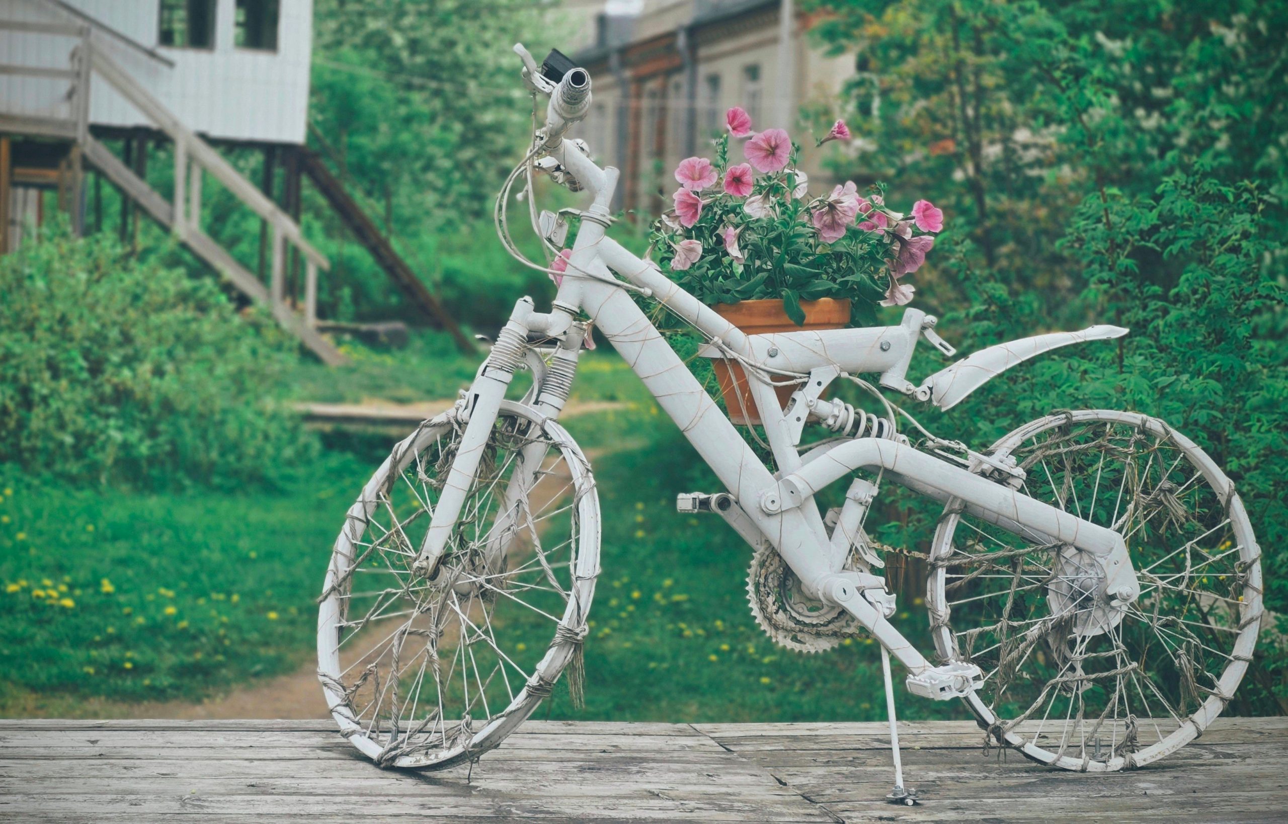 A creatively repurposed white bicycle serves as a unique planter in a lush garden setting.