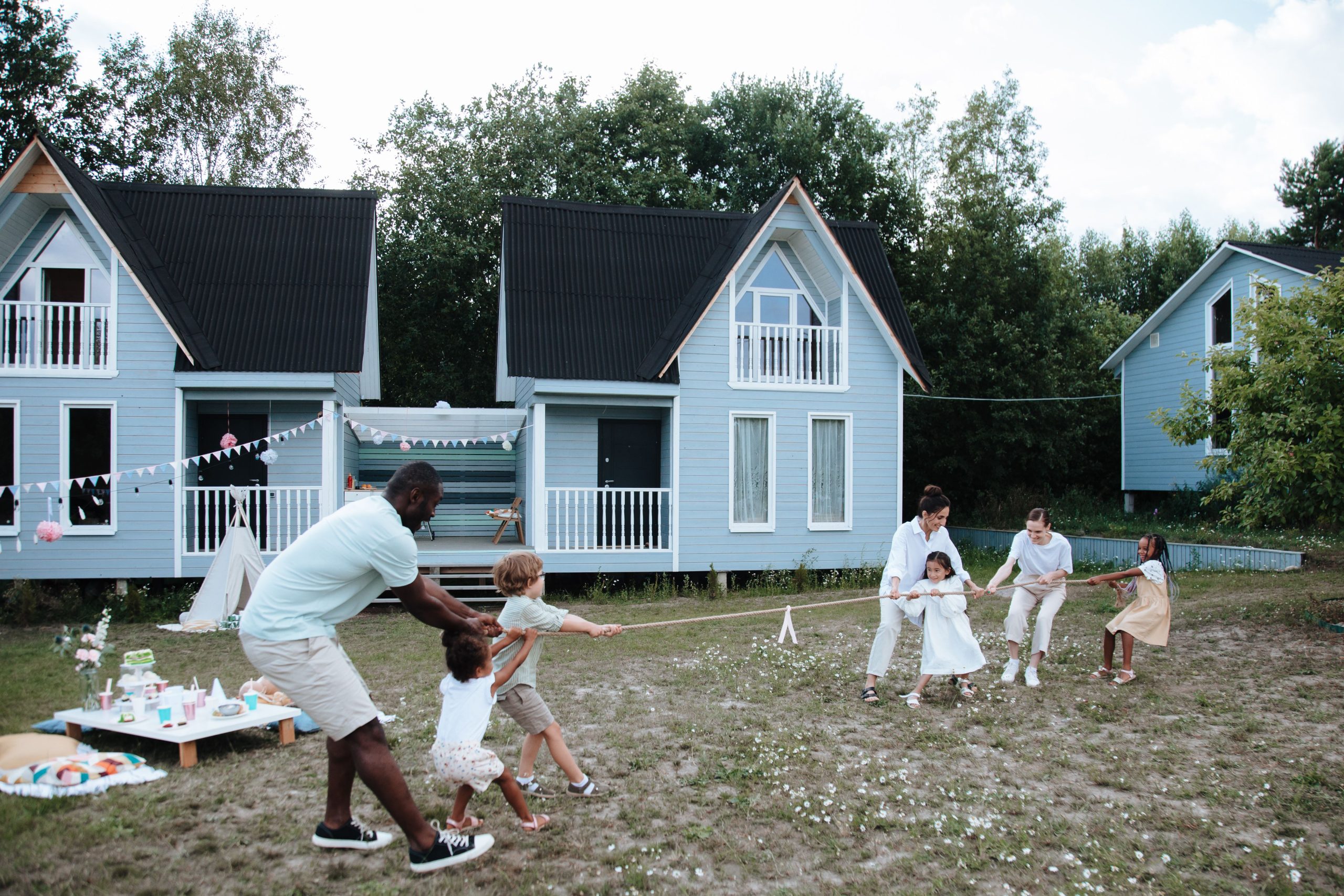 A diverse family plays tug of war outdoors near modern houses, enjoying a sunny day.