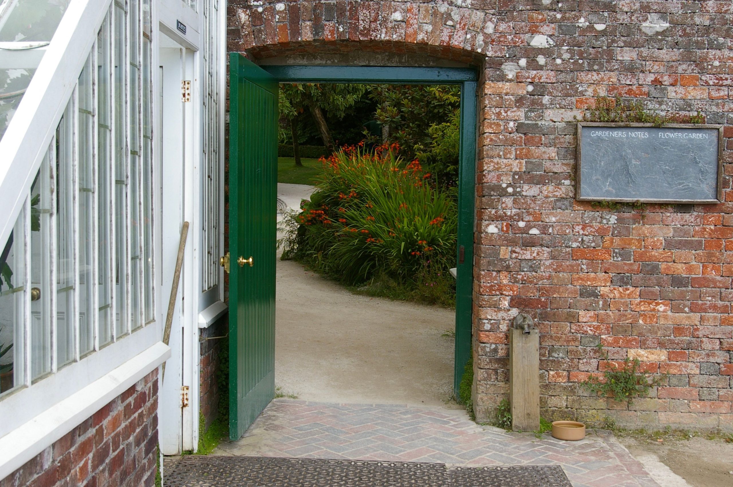 A green door opens to reveal a vibrant garden path bordered by red flowers and lush greenery.