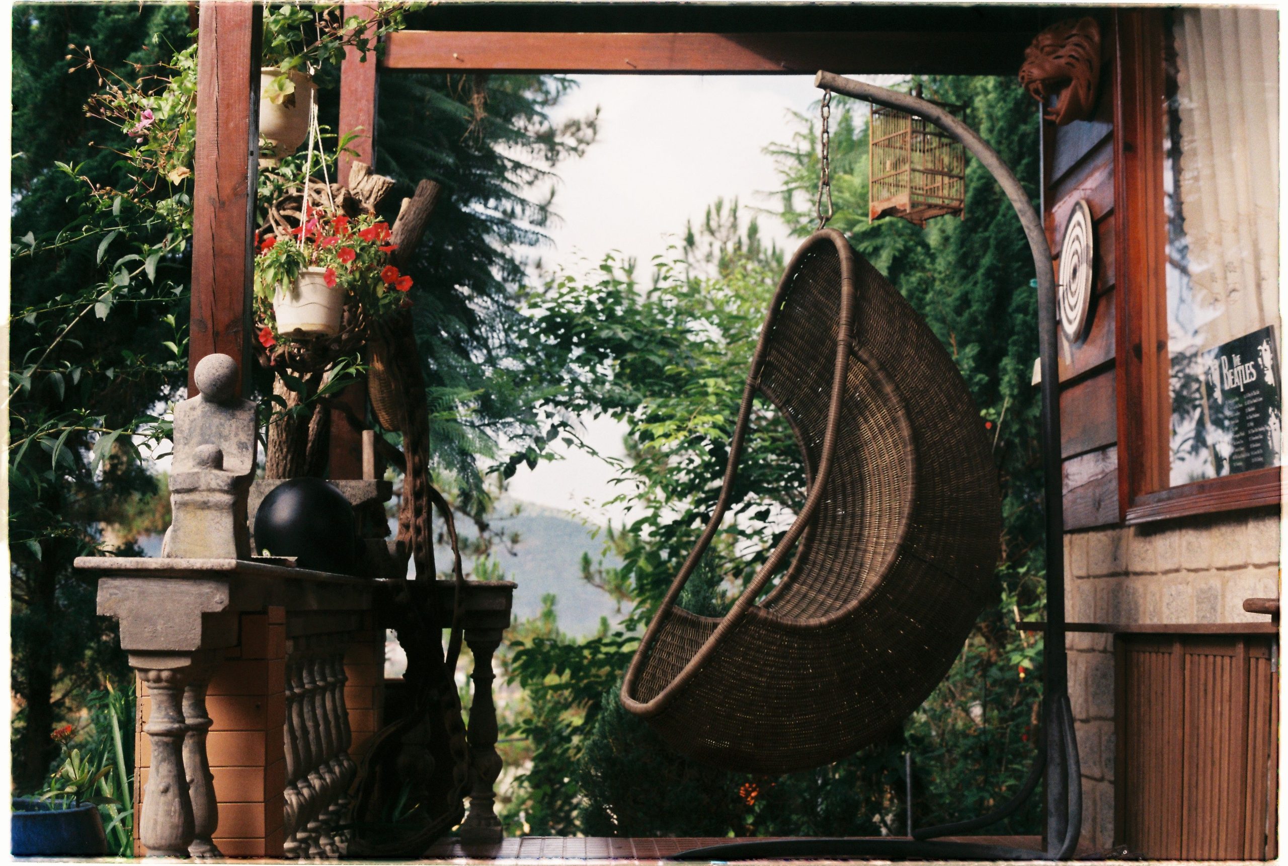 A rustic porch featuring a wicker hanging chair and vibrant flowers, perfect for a peaceful outdoor retreat.