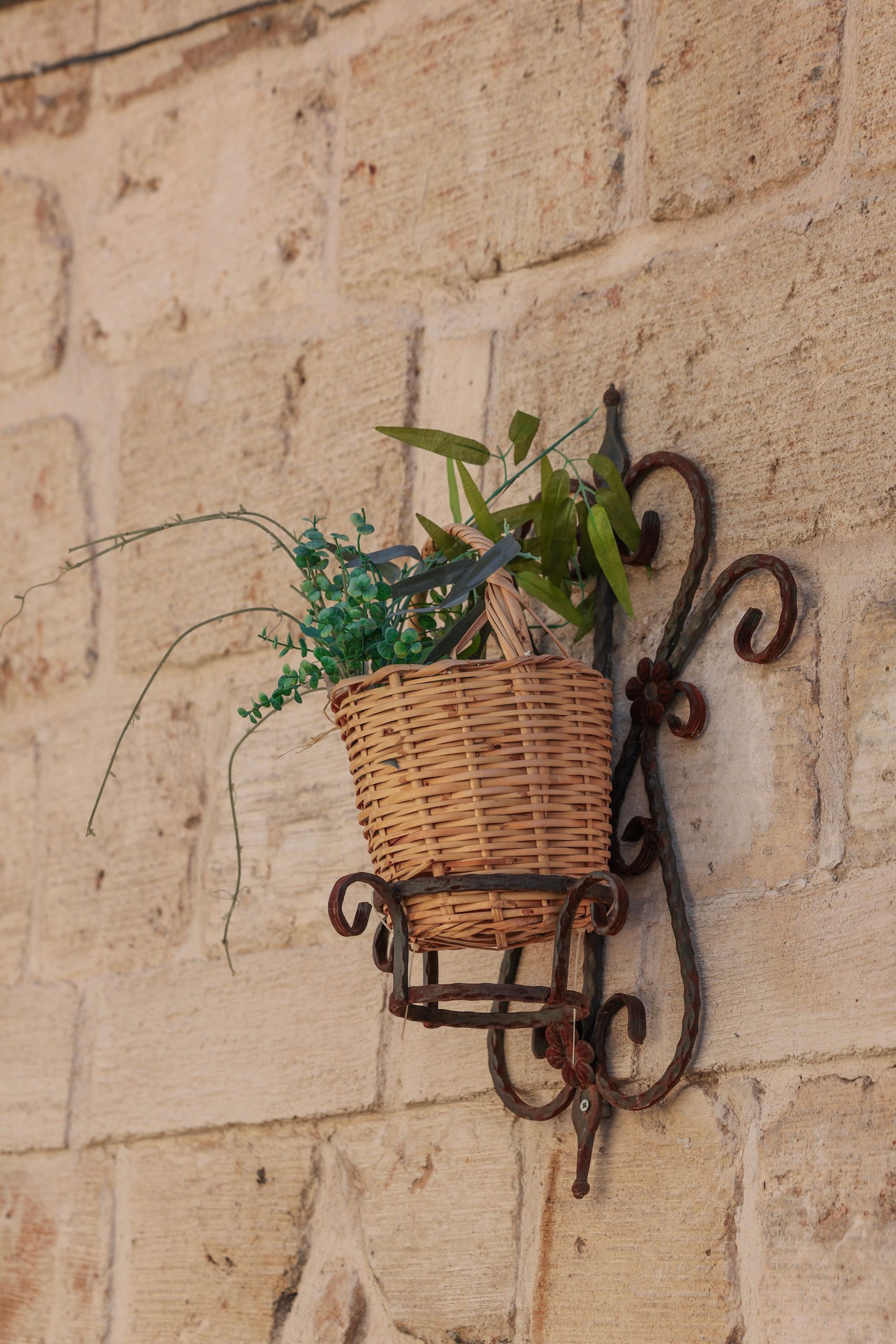 A rustic wicker flowerpot with green plants on a stone wall in Mardin, Türkiye.
