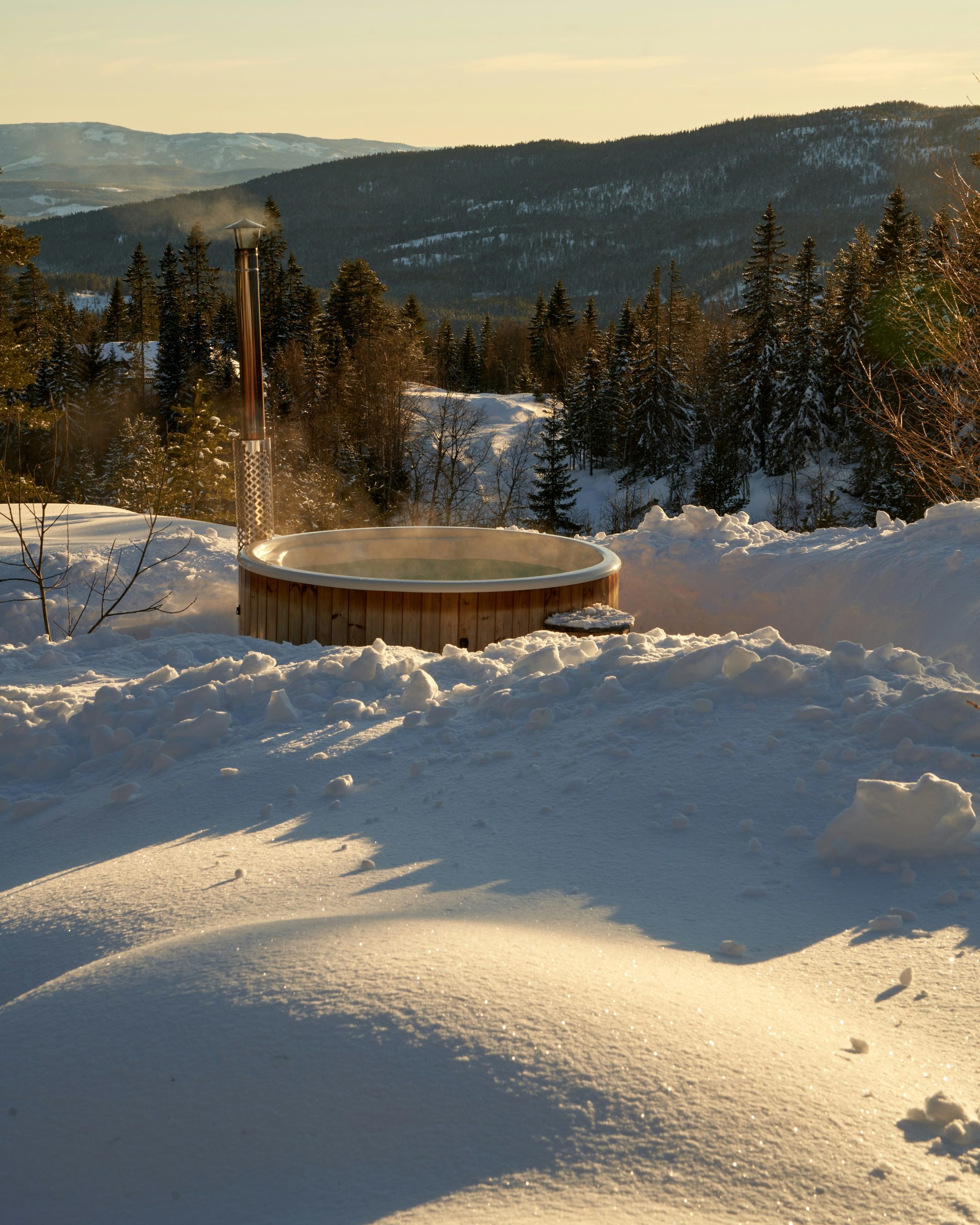 A rustic wooden hot tub steams invitingly beside a snow-dusted winter forest in Kroderen, Norway.