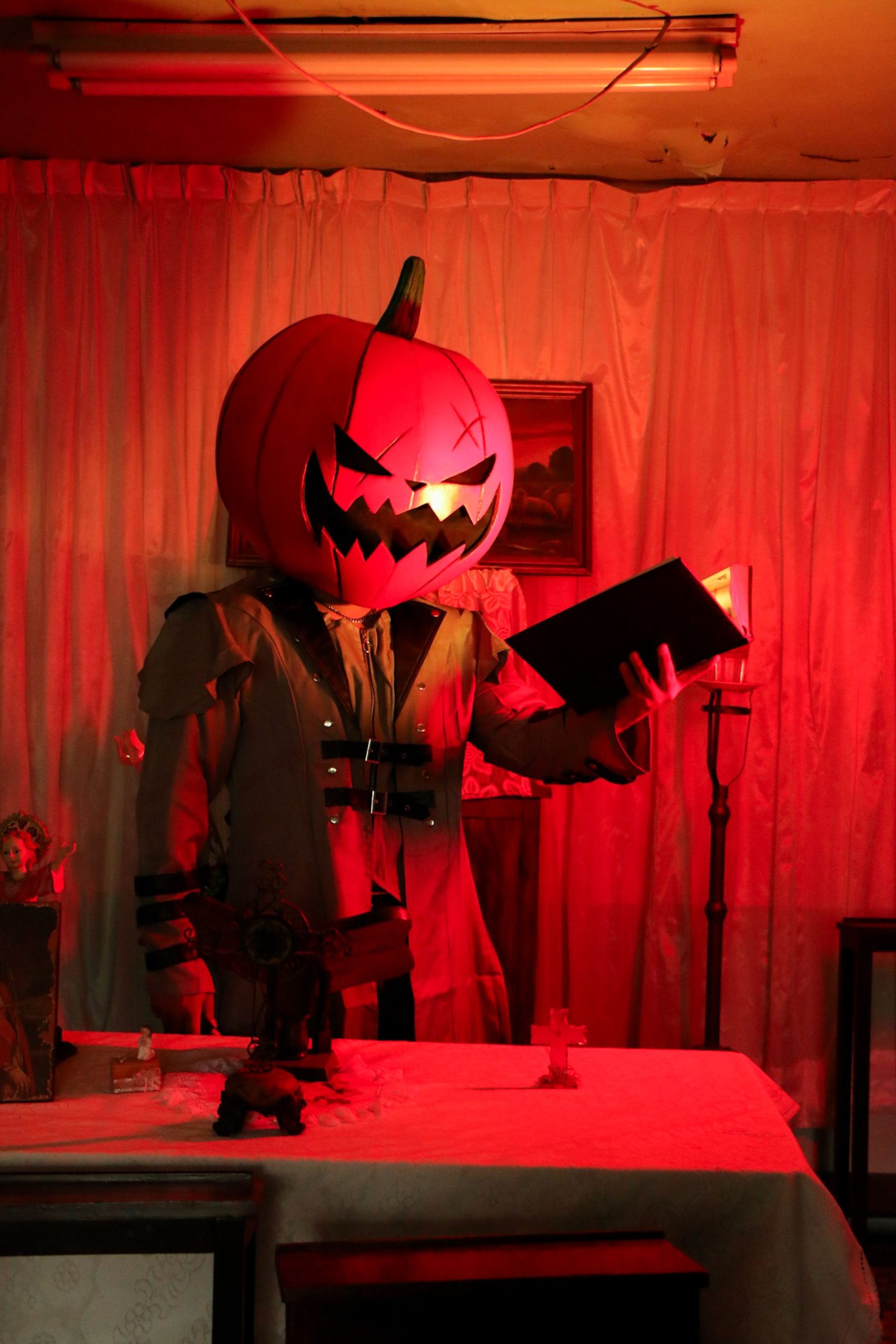A spooky Halloween figure with a pumpkin head in a dimly lit room, holding a book.