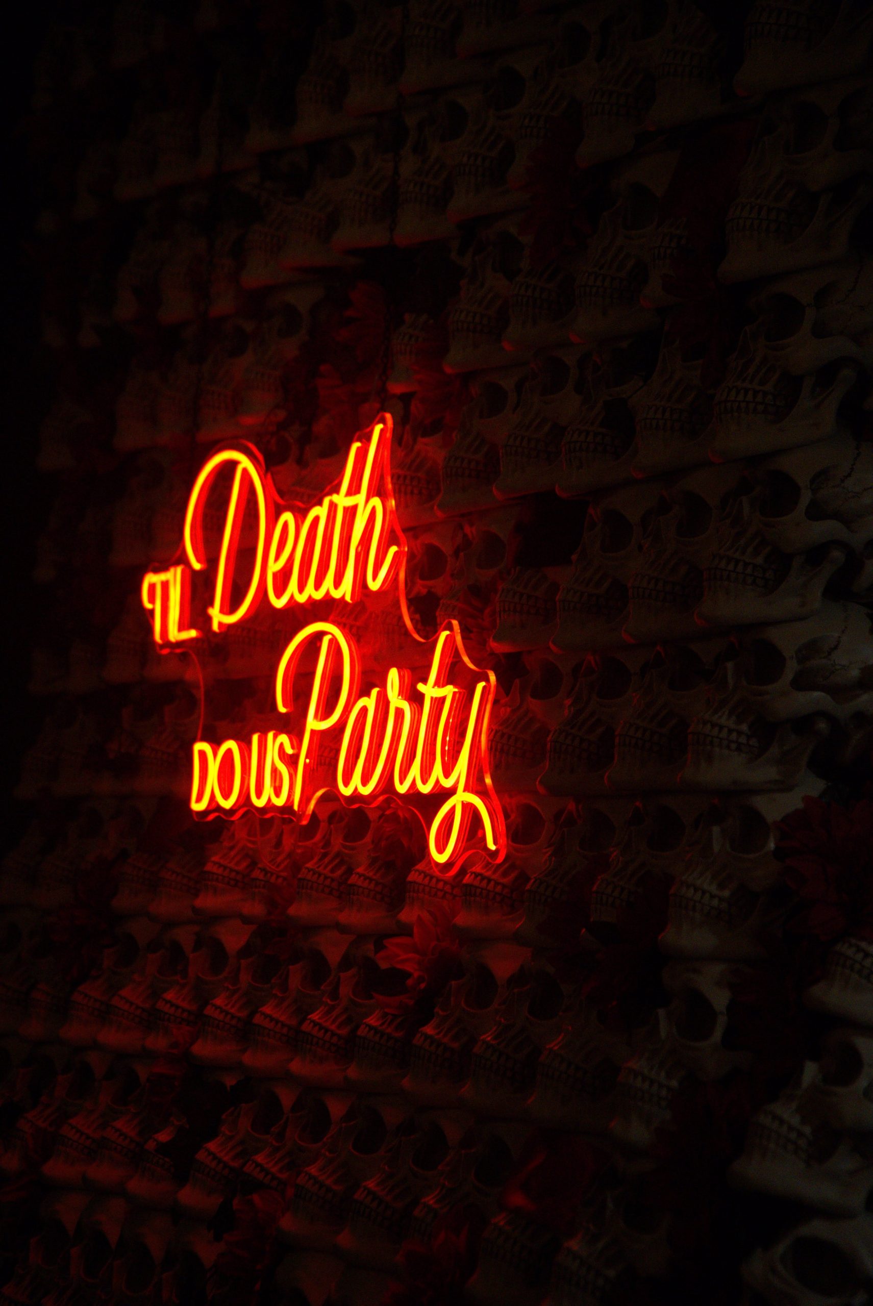 A striking neon sign 'Til Death Do Us Party' against a skull-themed wall, perfect for party themes.
