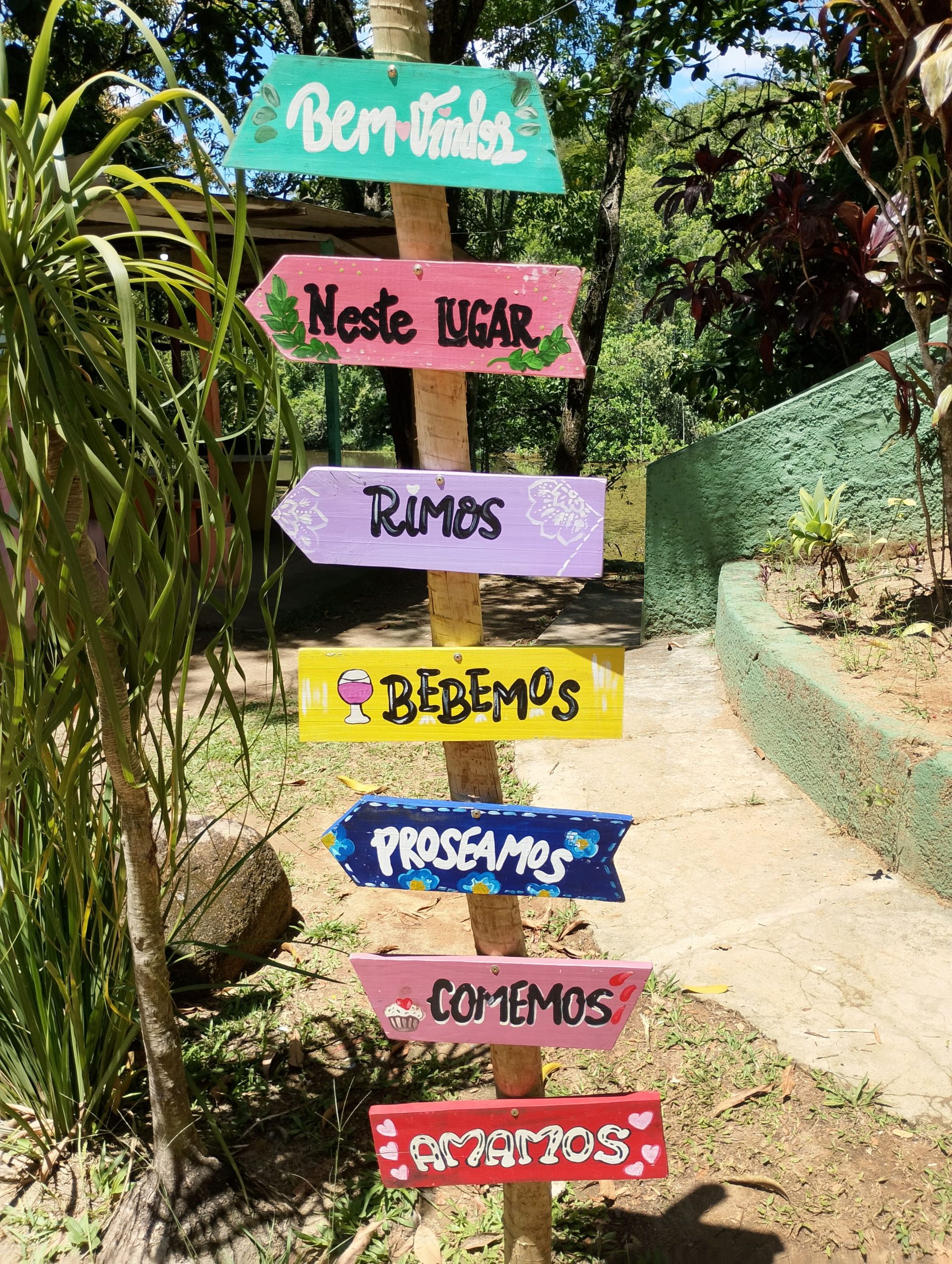 A vibrant signpost with welcoming and festive text in a sunny garden.